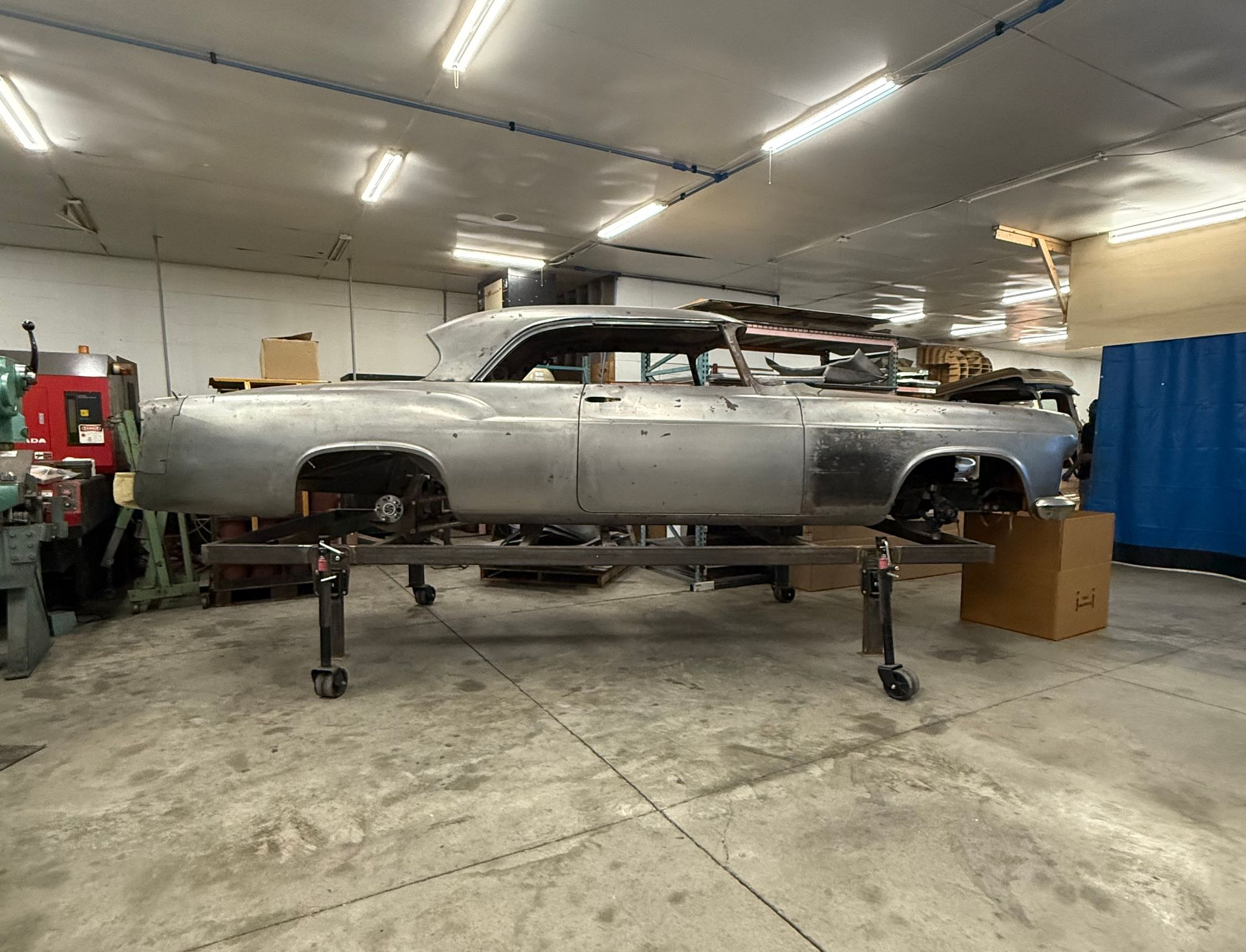 Silver classic car body on jack stands in a workshop garage, under restoration.