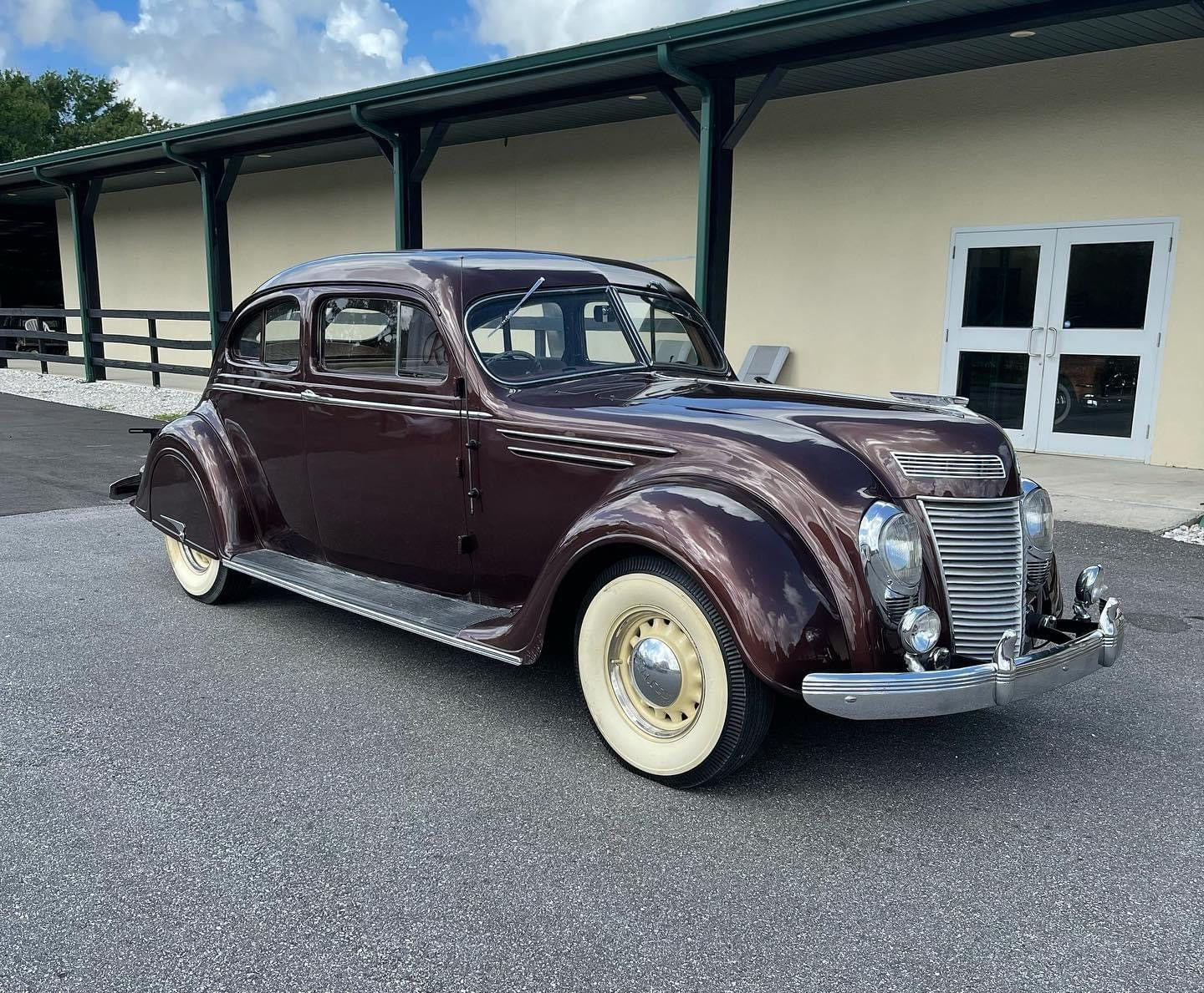 Vintage maroon coupe parked outside a cream building with a dark roof and white-trimmed windows
