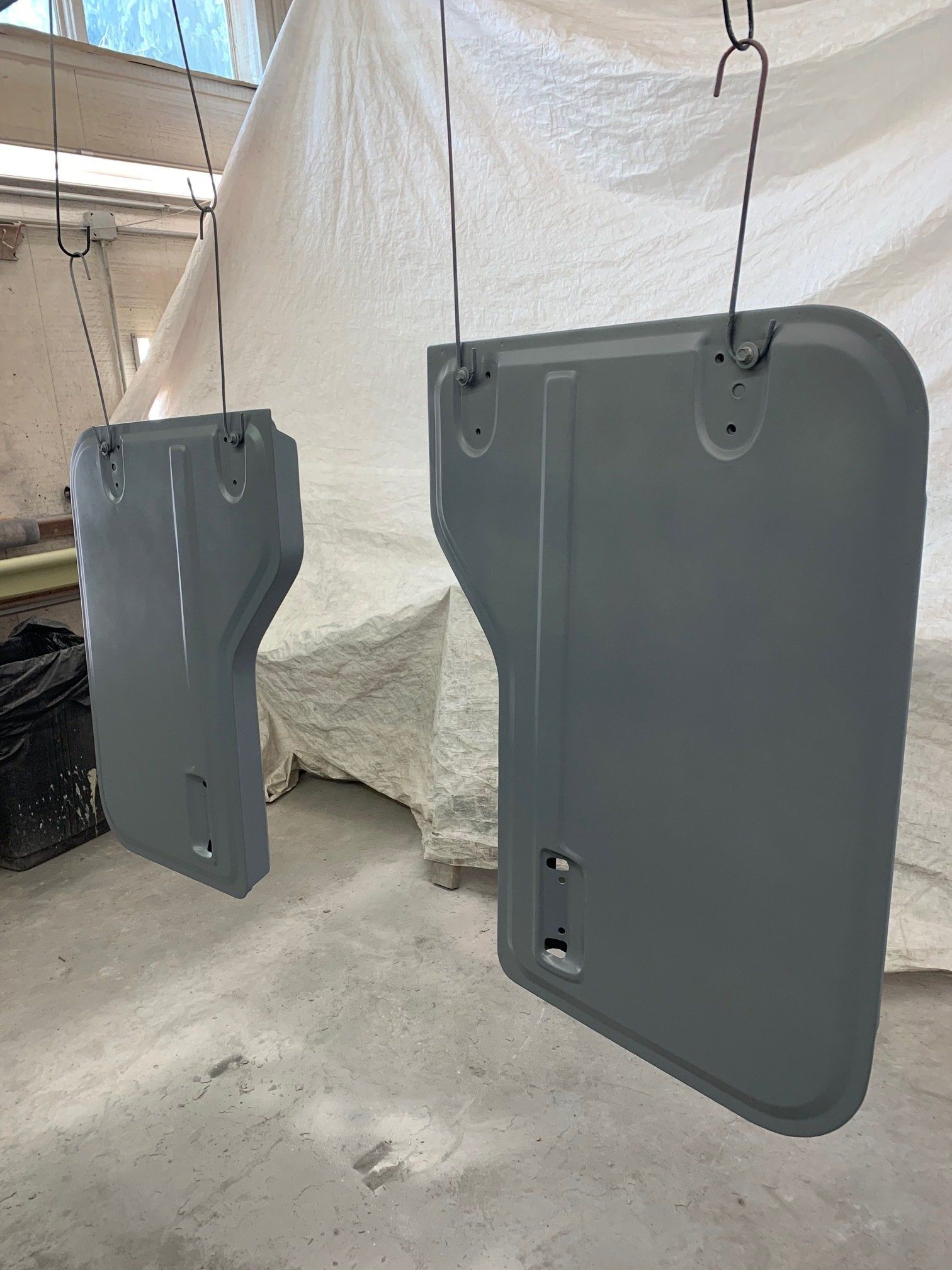 Two gray metal panels hanging from hooks in a workshop, one large and one smaller