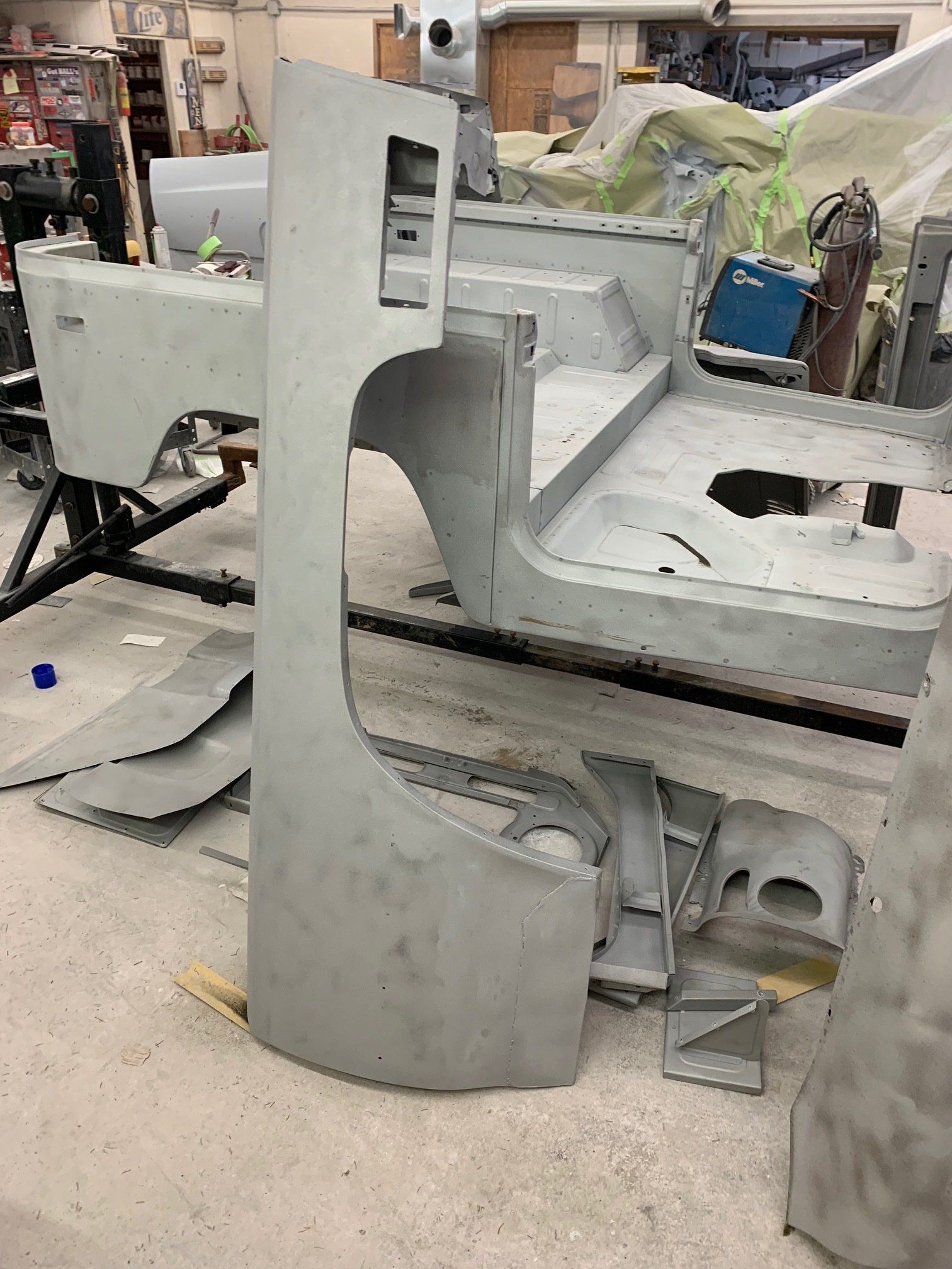 Large gray vehicle body shell in a workshop, with cutout sections and tools in the background