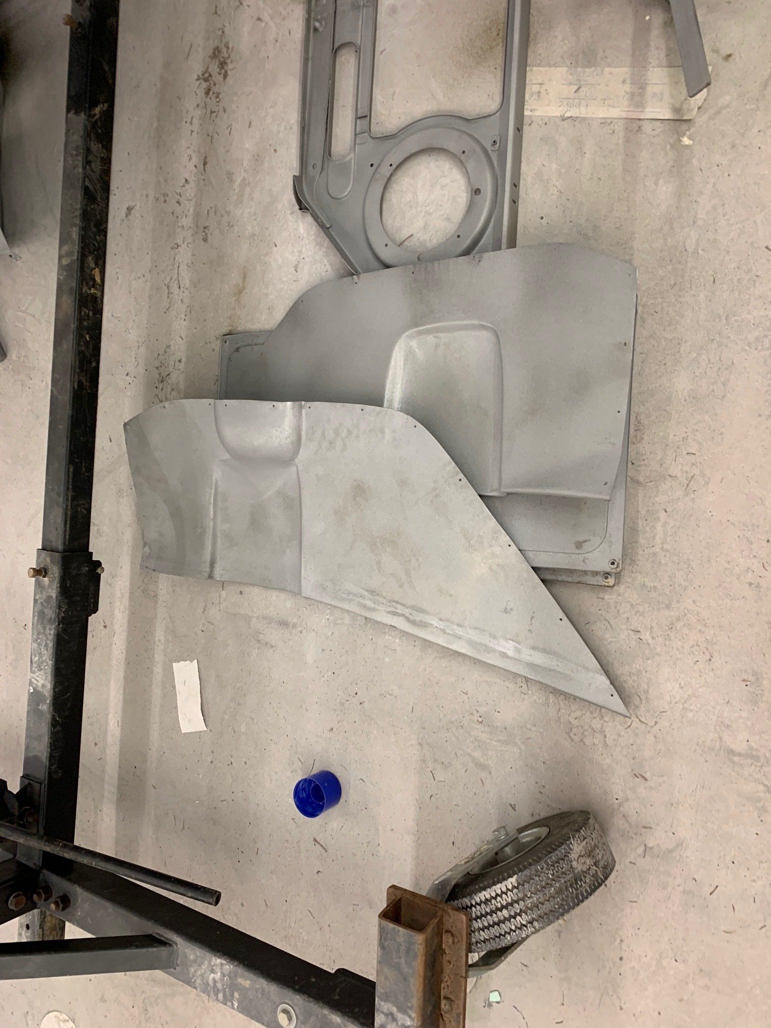 Assorted metal panels and parts laid on a concrete floor in a workshop