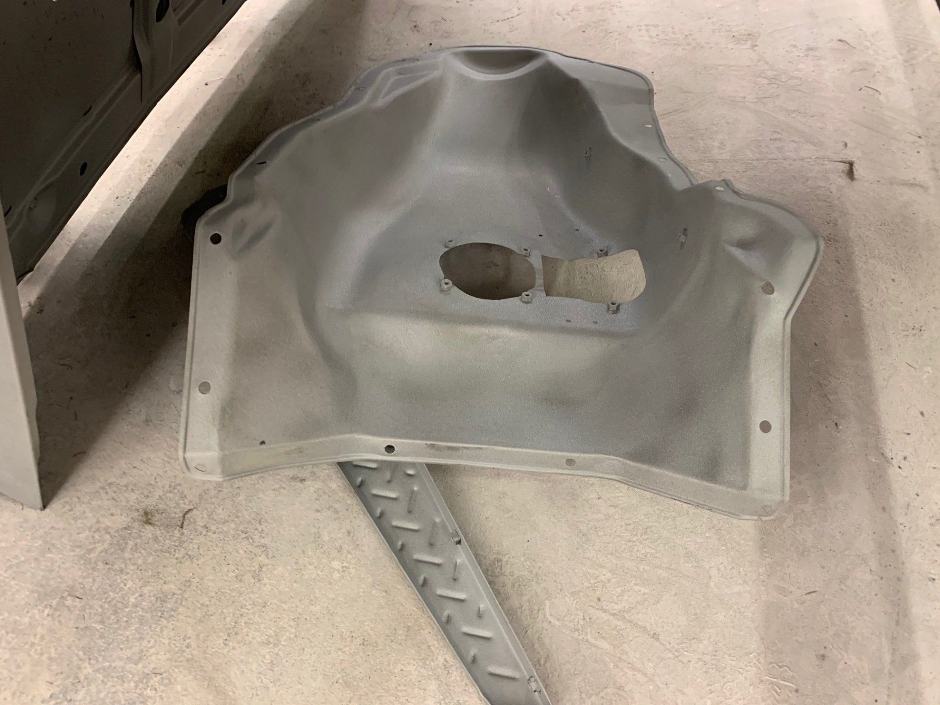 Gray plastic car interior panel with a cutout, lying on a concrete floor near a metal ramp.