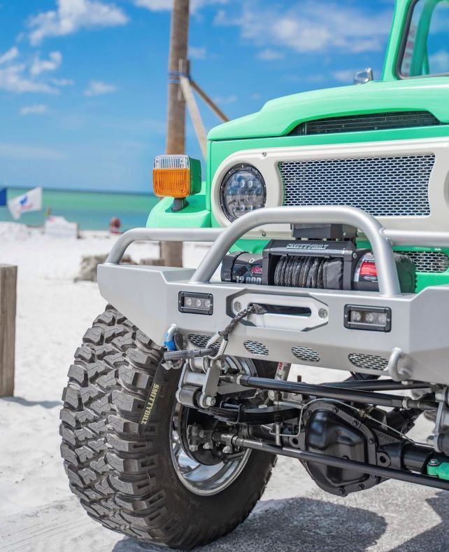 Bright green off-road truck front on a snowy beach, showing large tires and a silver bumper