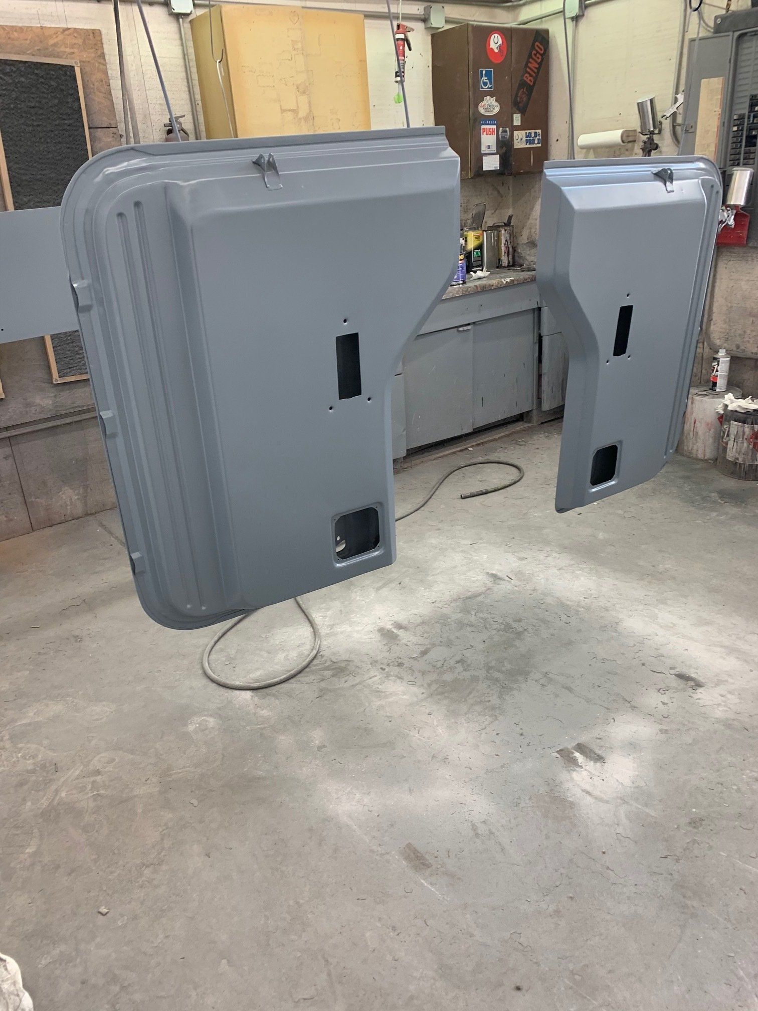 Two gray industrial cabinets in a workshop, with one leaning against a wall and the other standing nearby.