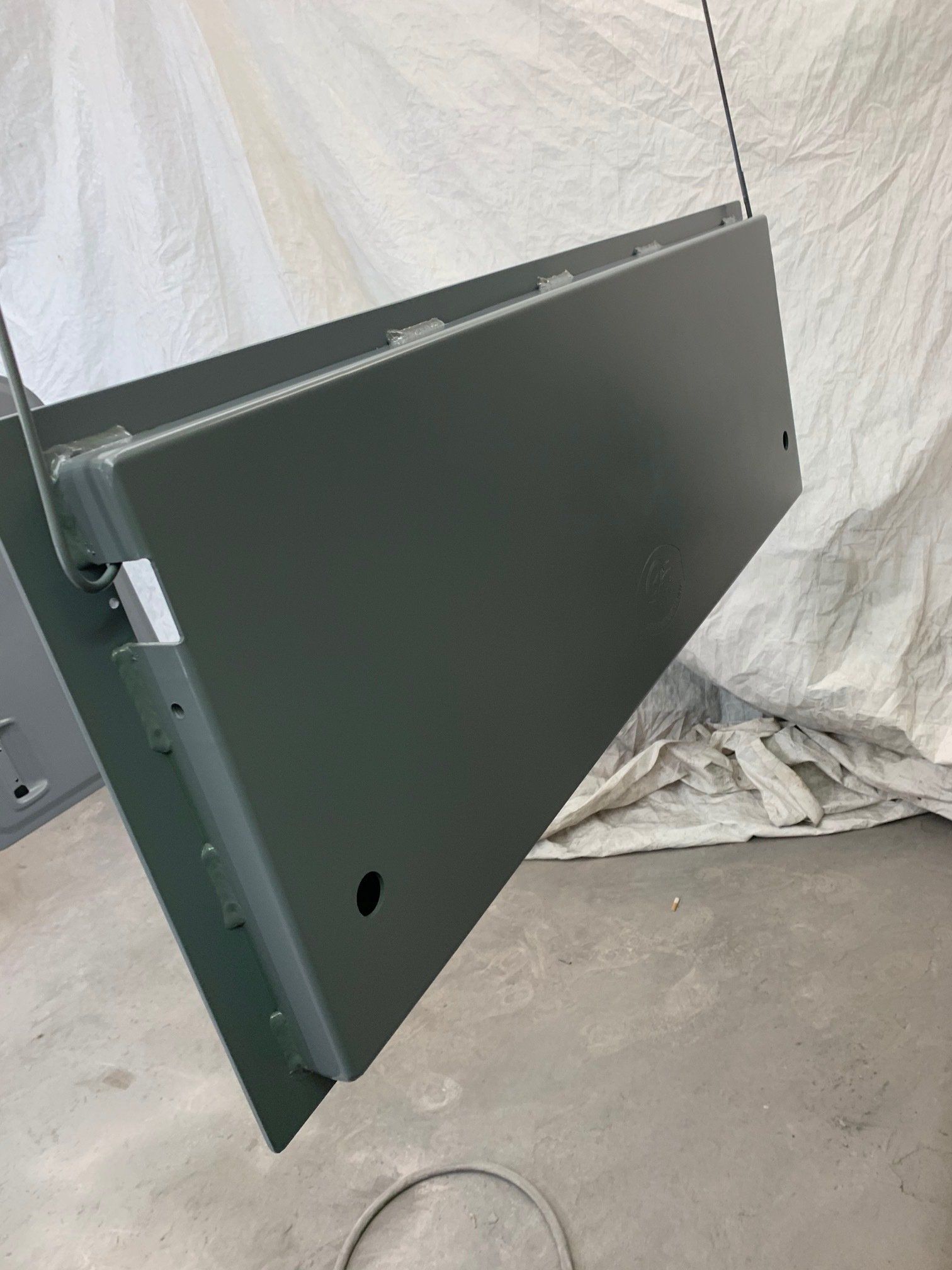 Large black metal panel hanging by wires in a workshop or paint booth