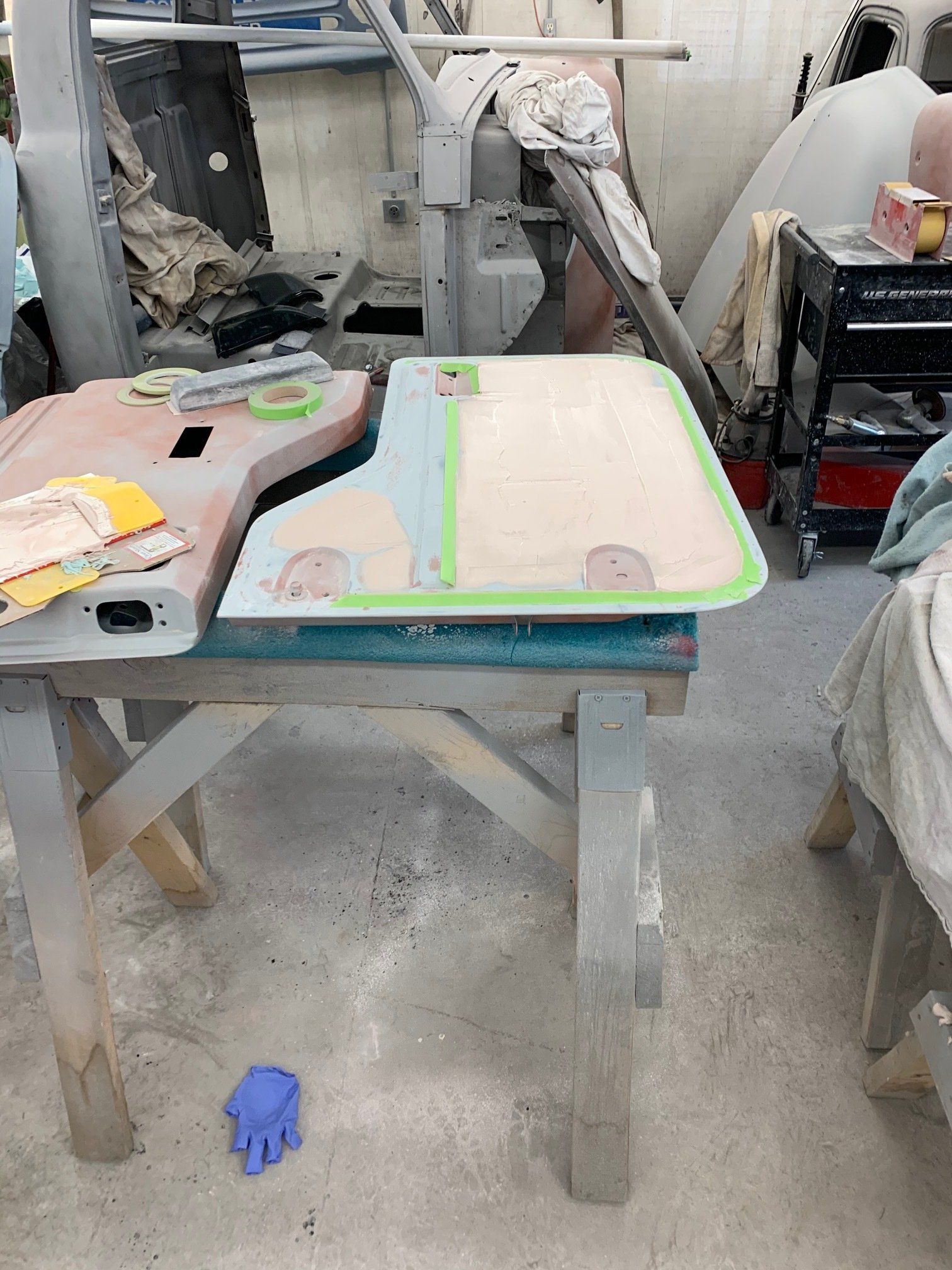 Dusty workbench with a colorful cutting mat, tools, and a blue glove on the floor in a workshop