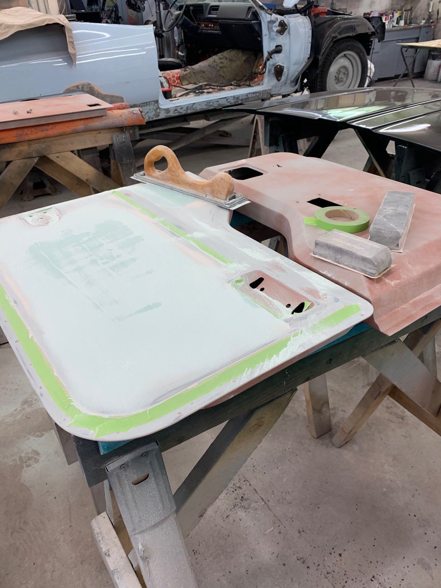 Two painted car body panels on sawhorses in a workshop, one light green and one pink.