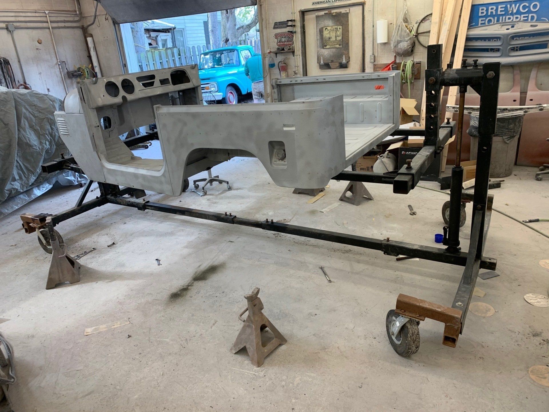 Gray car body on a wheeled frame in an auto shop, with snow on the floor and tools nearby