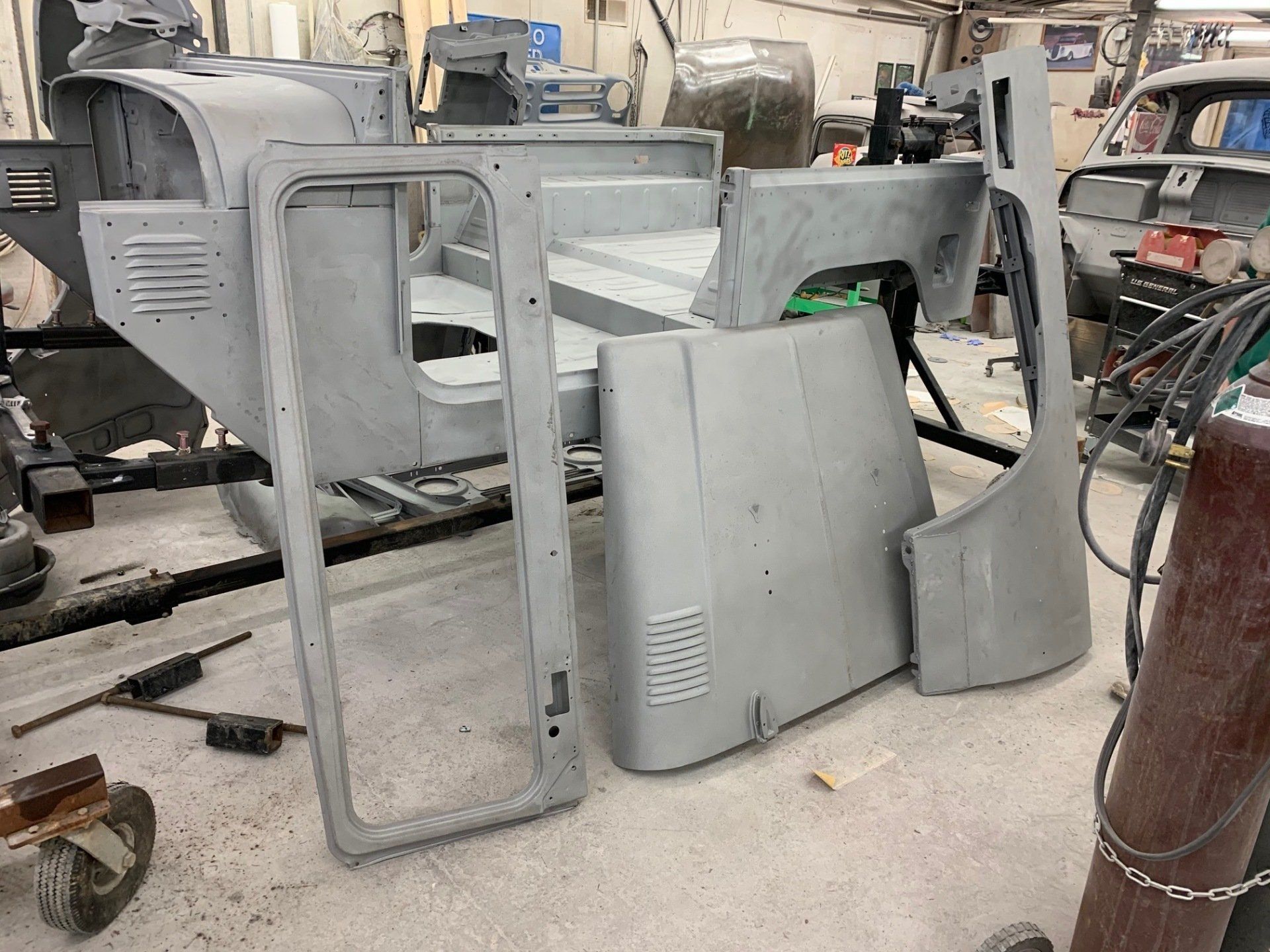 Gray car body panels and door frames stacked in a workshop garage.