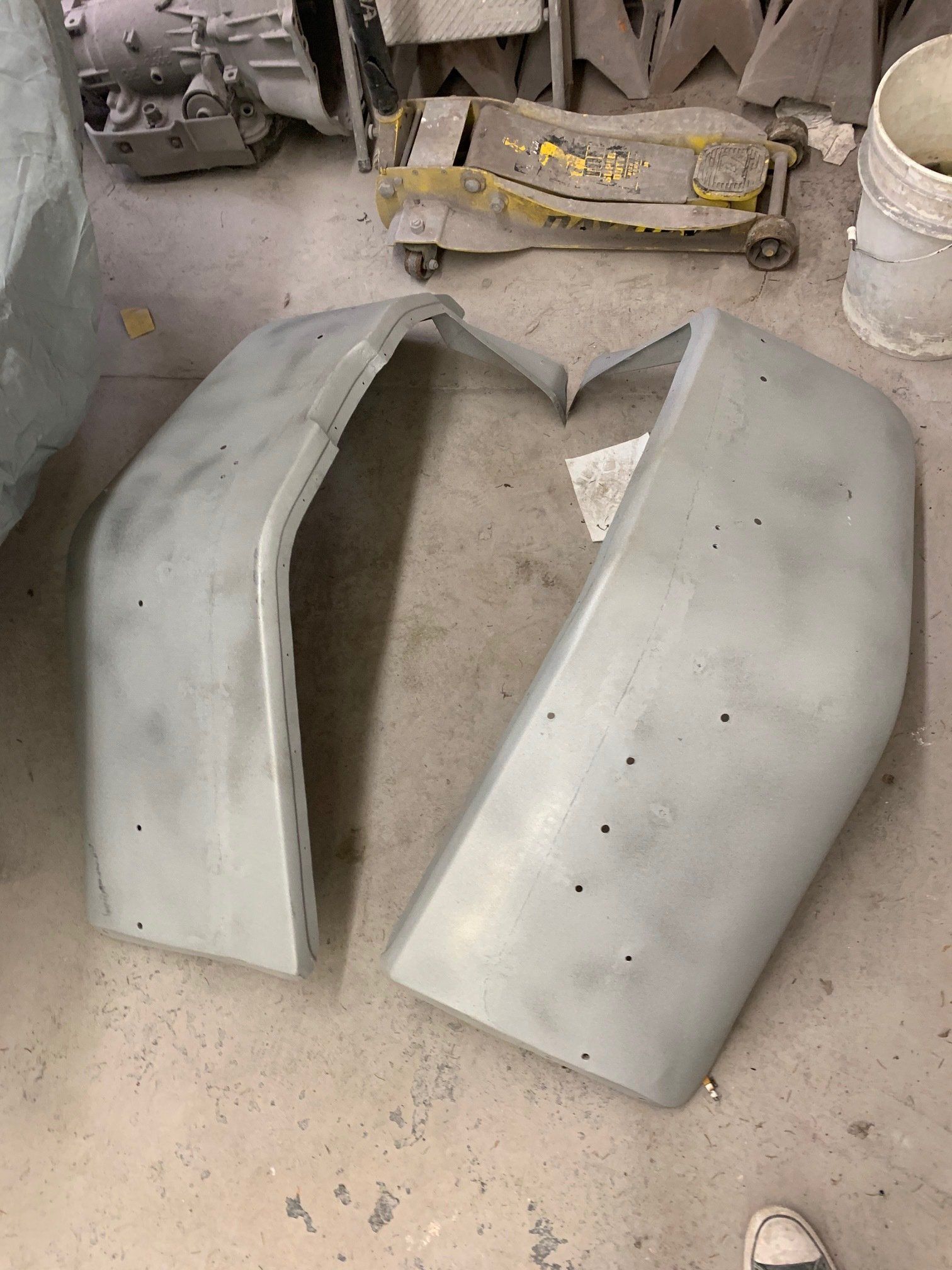 Two gray car body panels leaning on a dusty workshop floor.