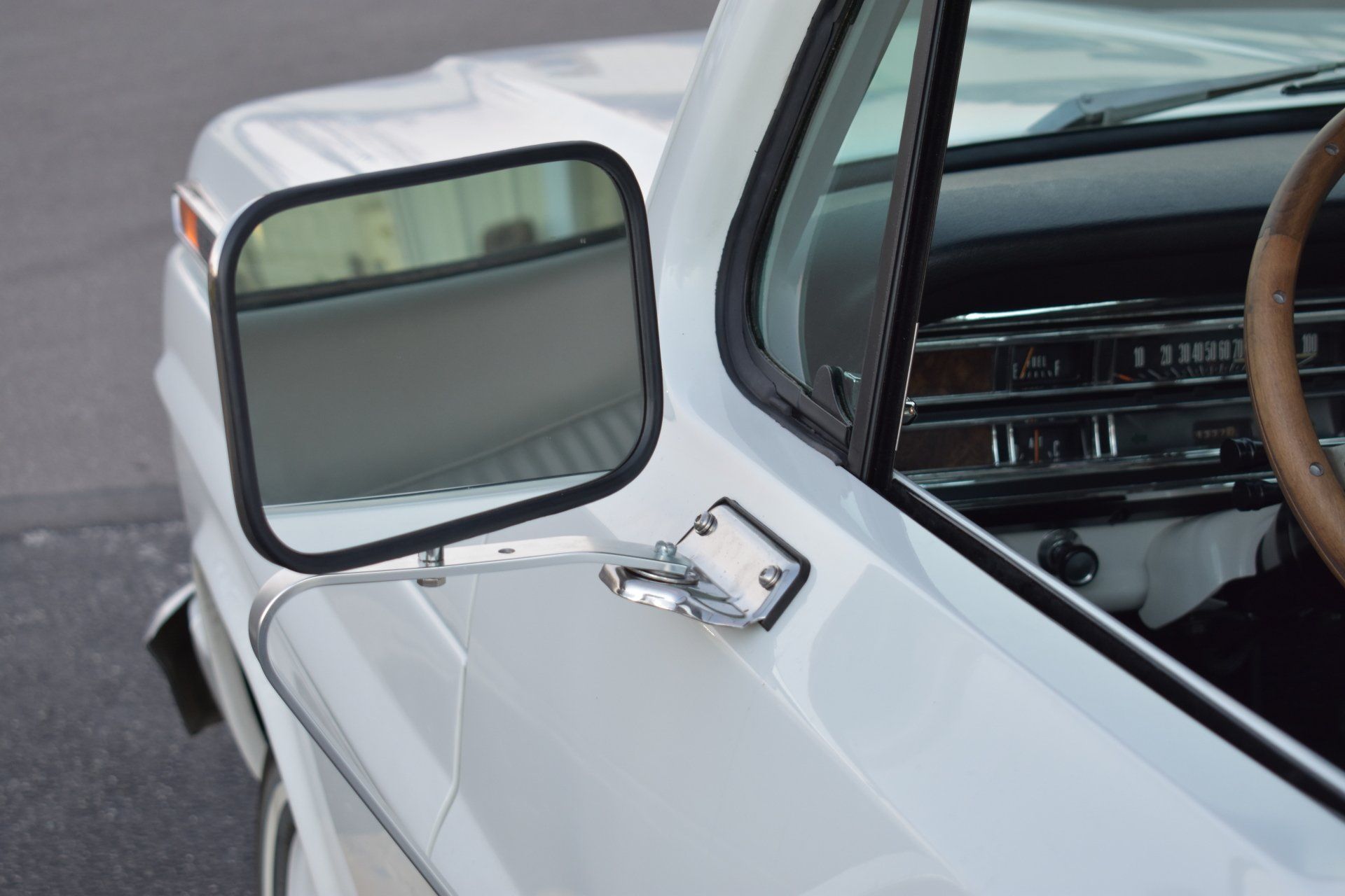 Close-up of a white car’s side mirror and door on a road, with a visible chrome mirror mount