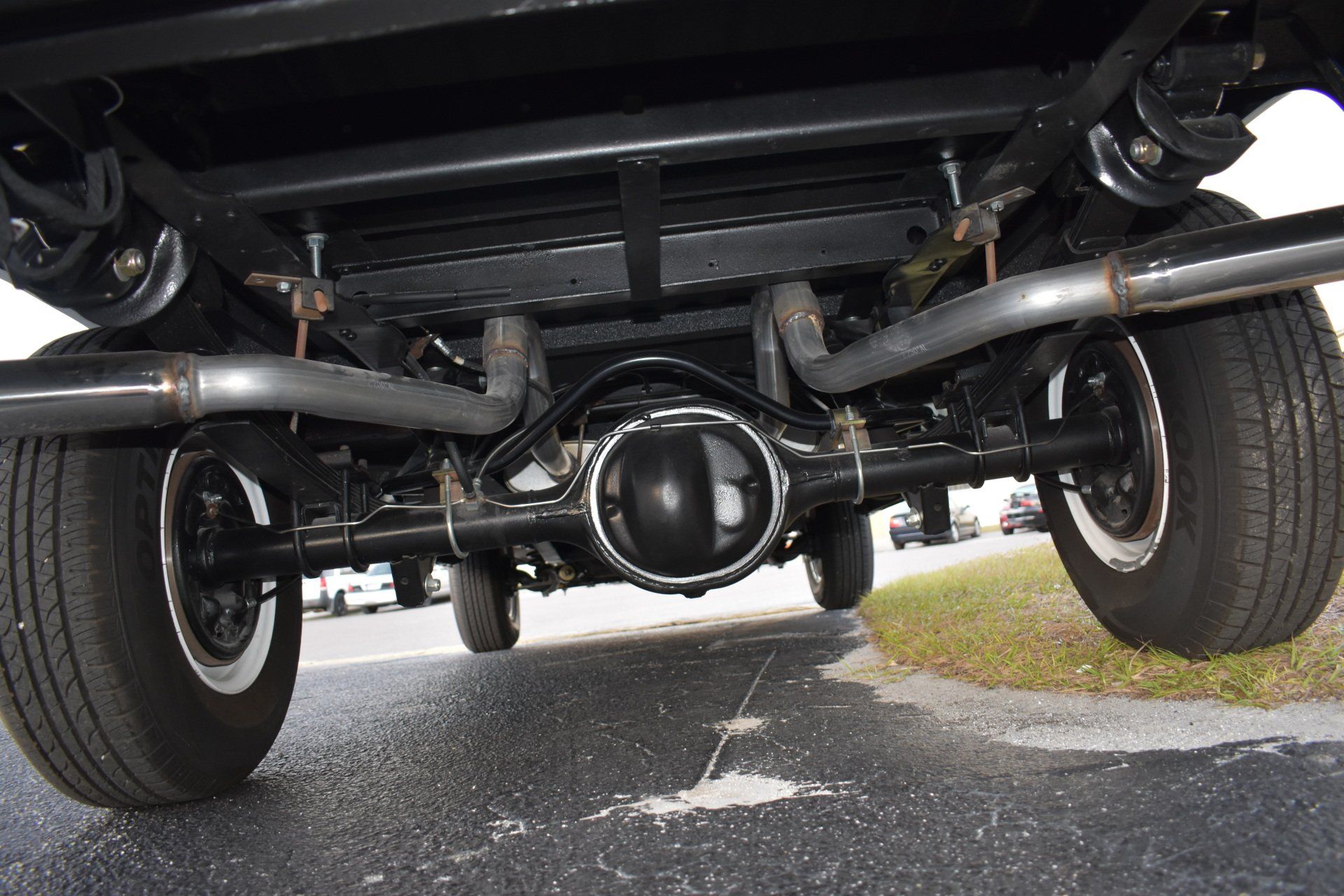 Undercarriage of a vehicle showing rear axle, suspension, and exhaust on a road surface