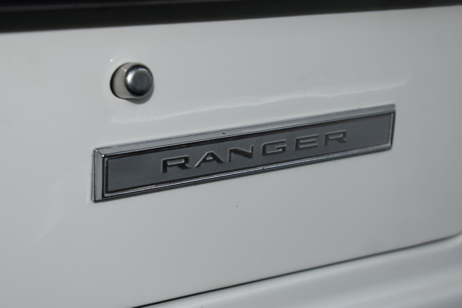 Close-up of a white truck tailgate with a chrome “RANGER” badge and key lock.
