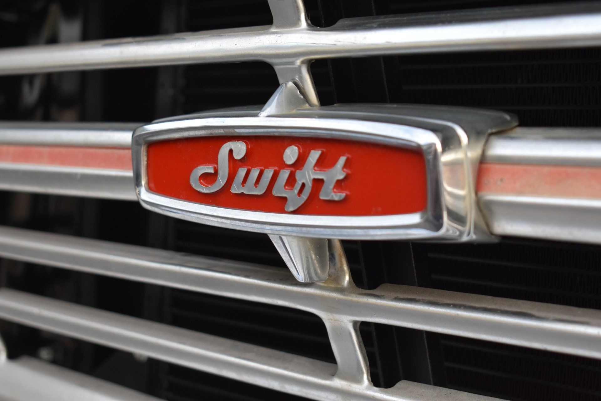 Close-up of a red Swift car grille emblem on chrome bars