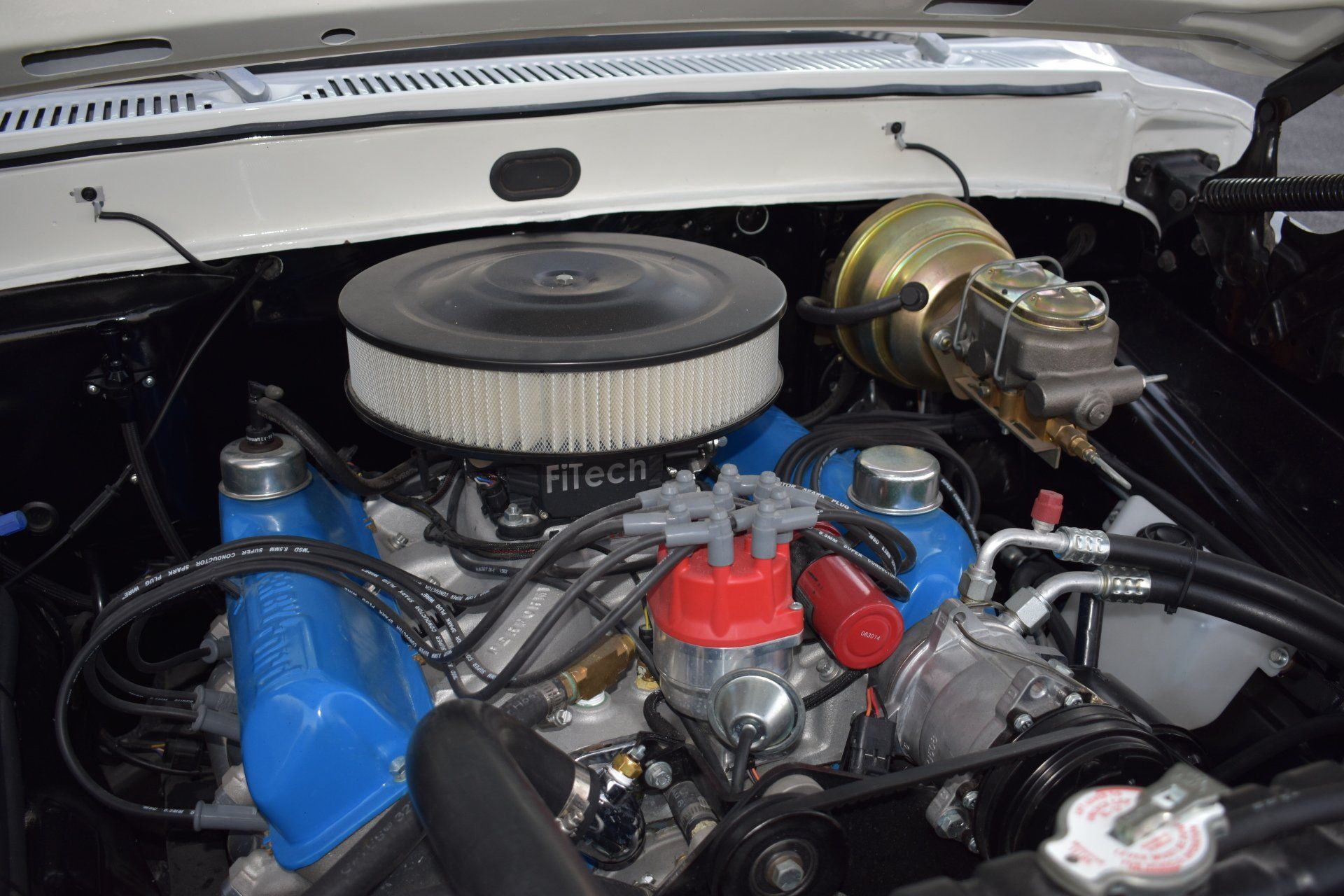 Classic car engine bay with chrome air filter, blue intake tubing, and red ignition components