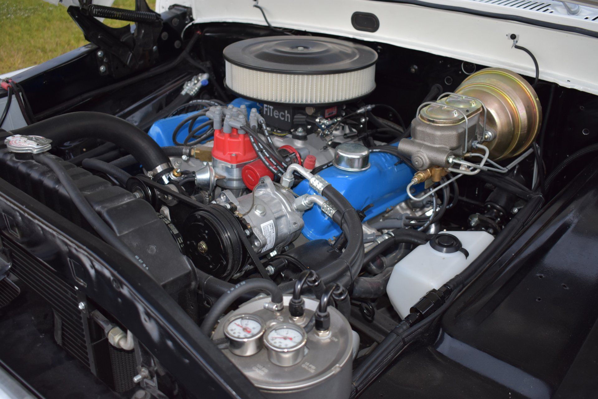 Classic car engine bay with blue engine, chrome air filter, and polished components under the hood