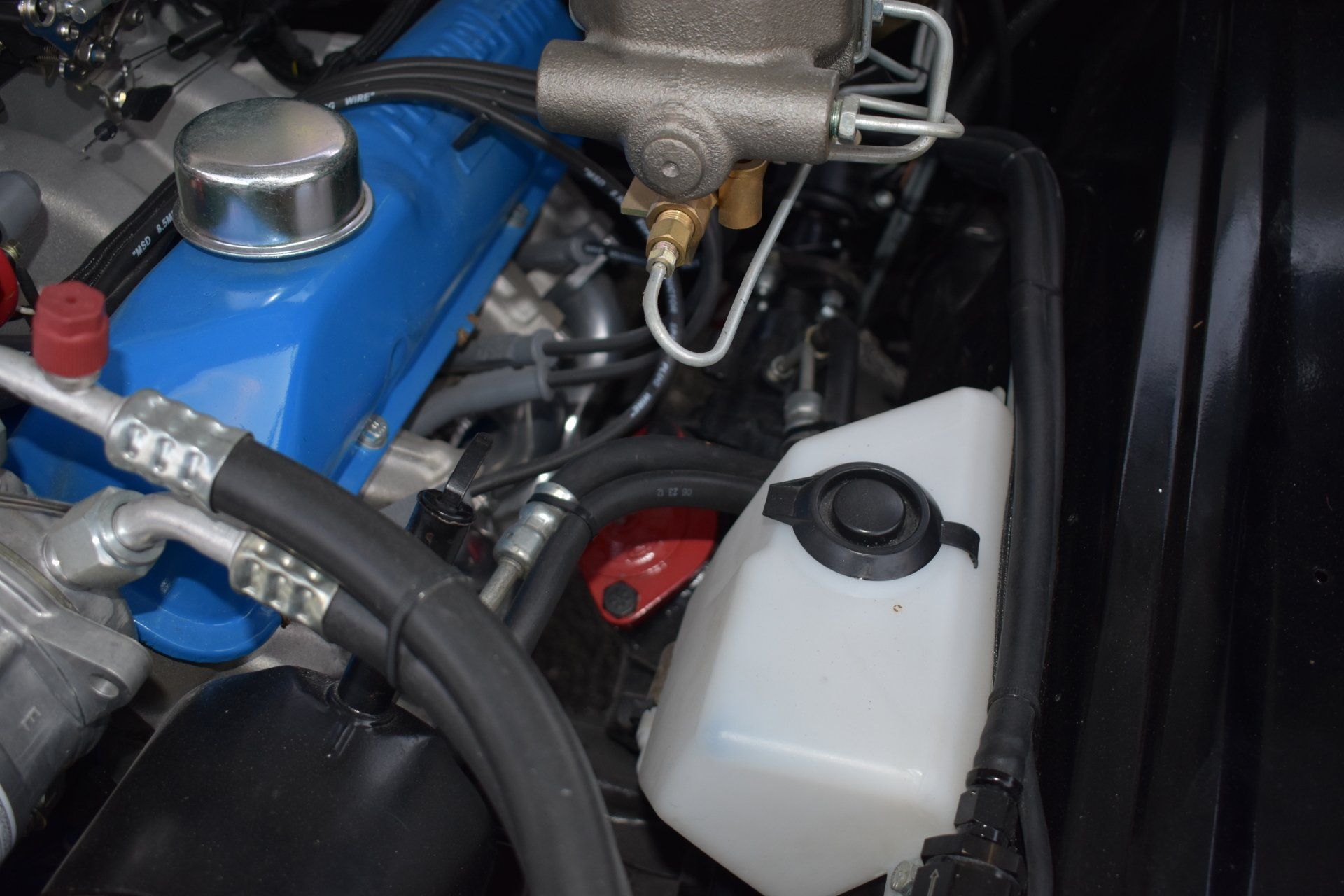 Car engine bay with blue engine cover, black hoses, and white fluid reservoir