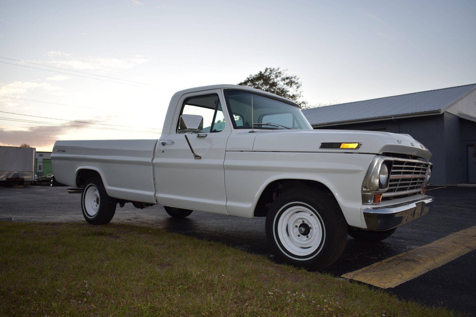 White vintage pickup truck parked beside a barn at sunset