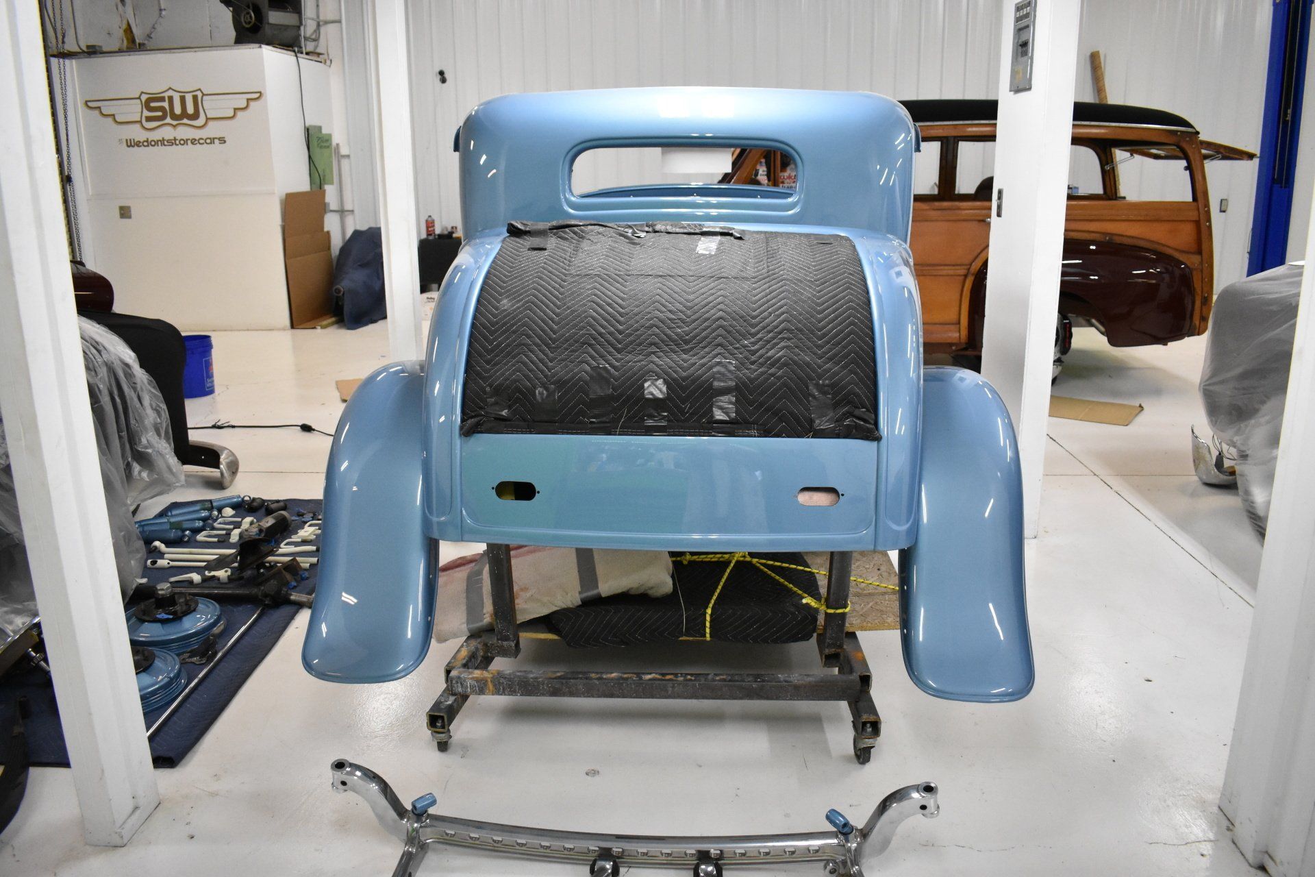 Light blue car body shell on a stand in a workshop, with tools and parts around it