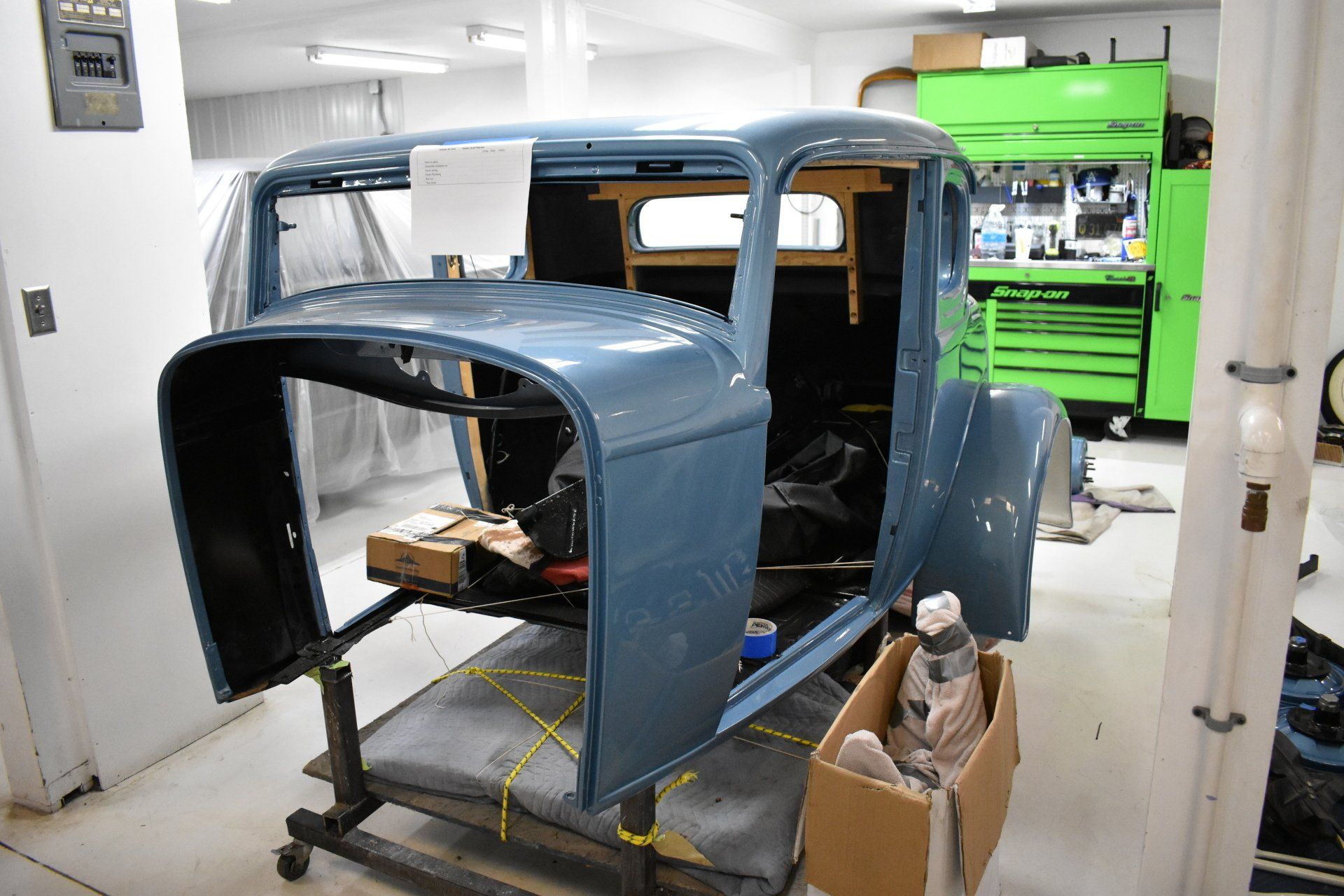 Blue truck body shell in an auto shop, with tools and parts around it on a lift platform.