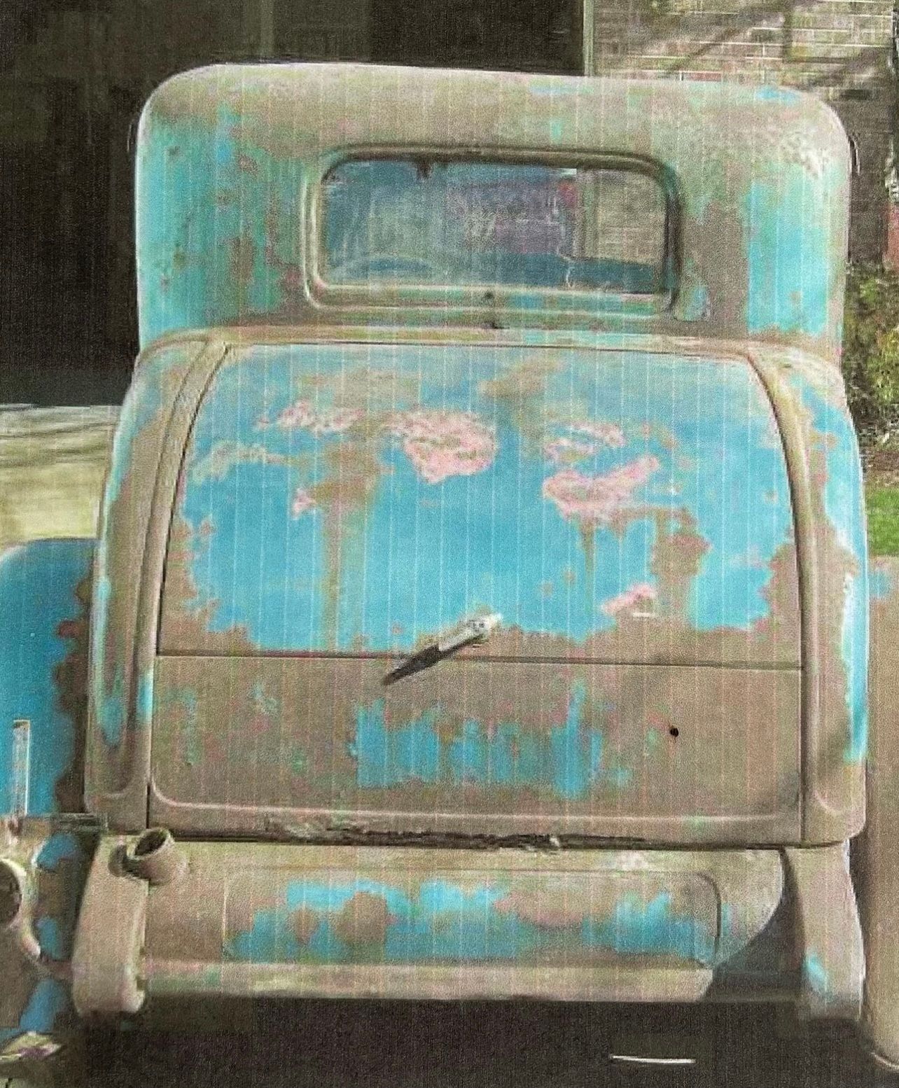 Weathered turquoise vintage vehicle front with chipped paint and a rectangular windshield.