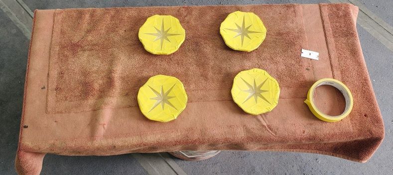 Four yellow paper flowers and a roll of tape on a brown towel-covered surface