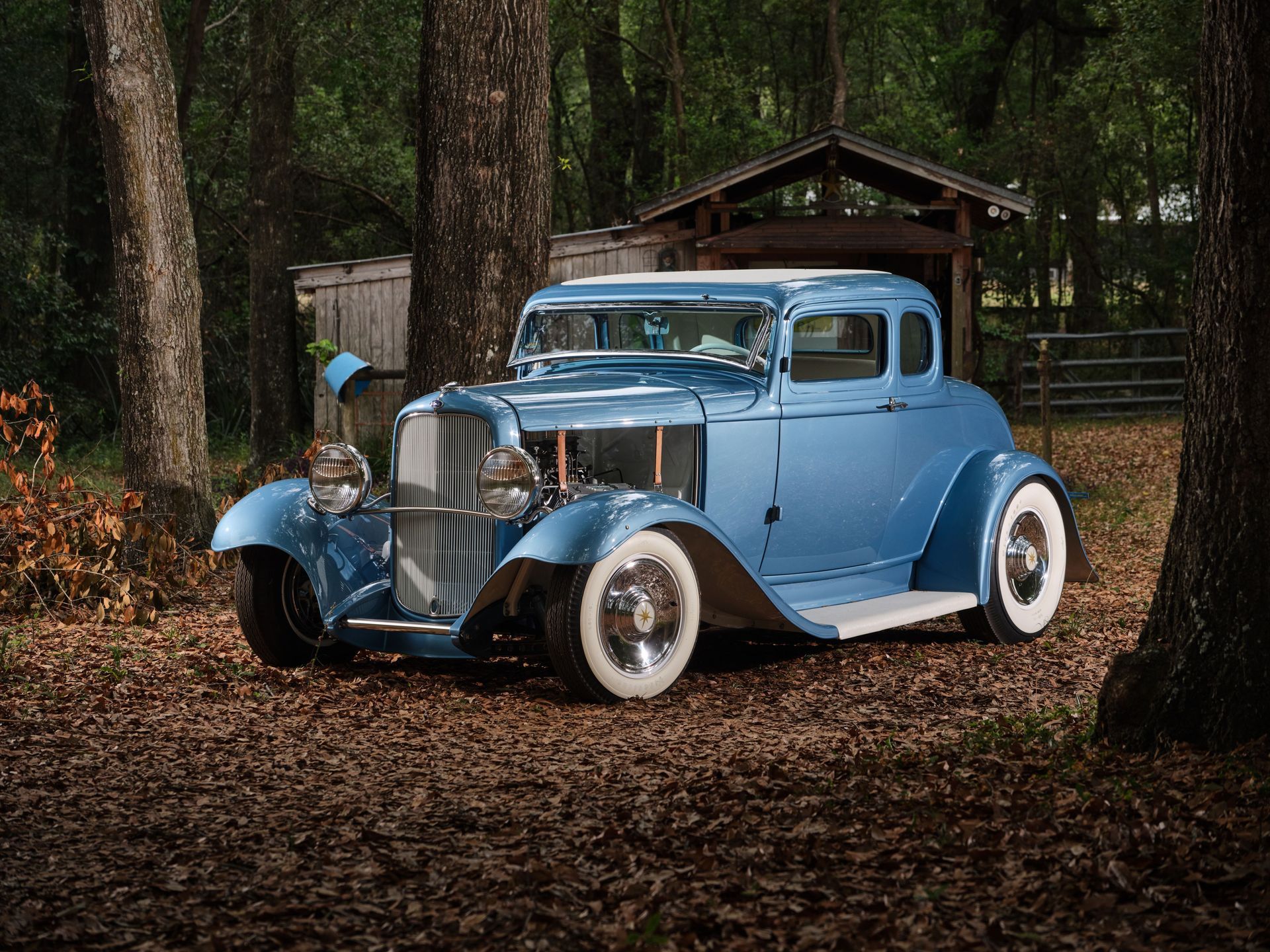 Light blue vintage car parked among trees in a wooded area