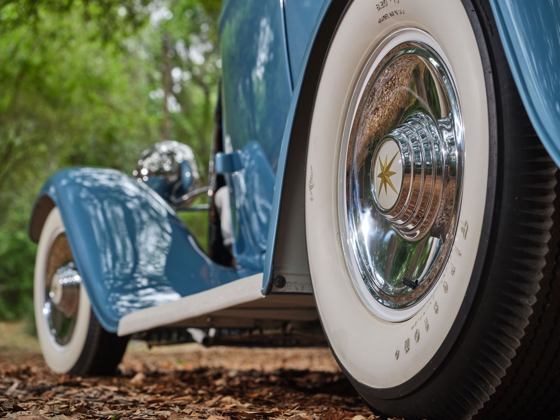 Close-up of a blue vintage car with whitewall tires on a gravel road