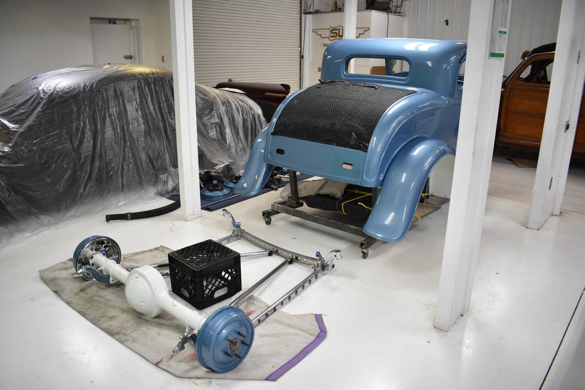 Blue vintage car body in a white workshop, with parts and tools on the floor nearby
