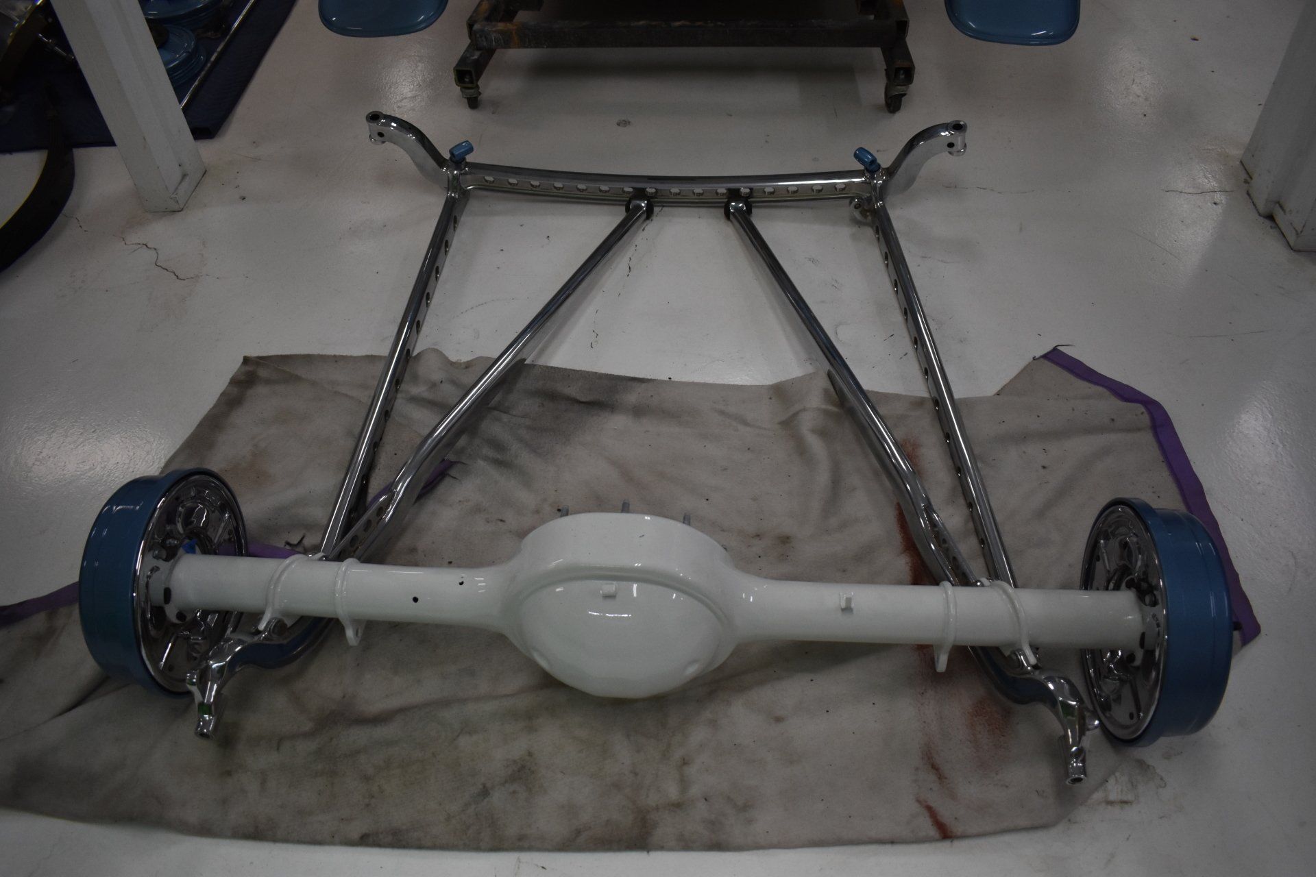 Car rear axle and differential on a workshop floor, with metal suspension arms attached.