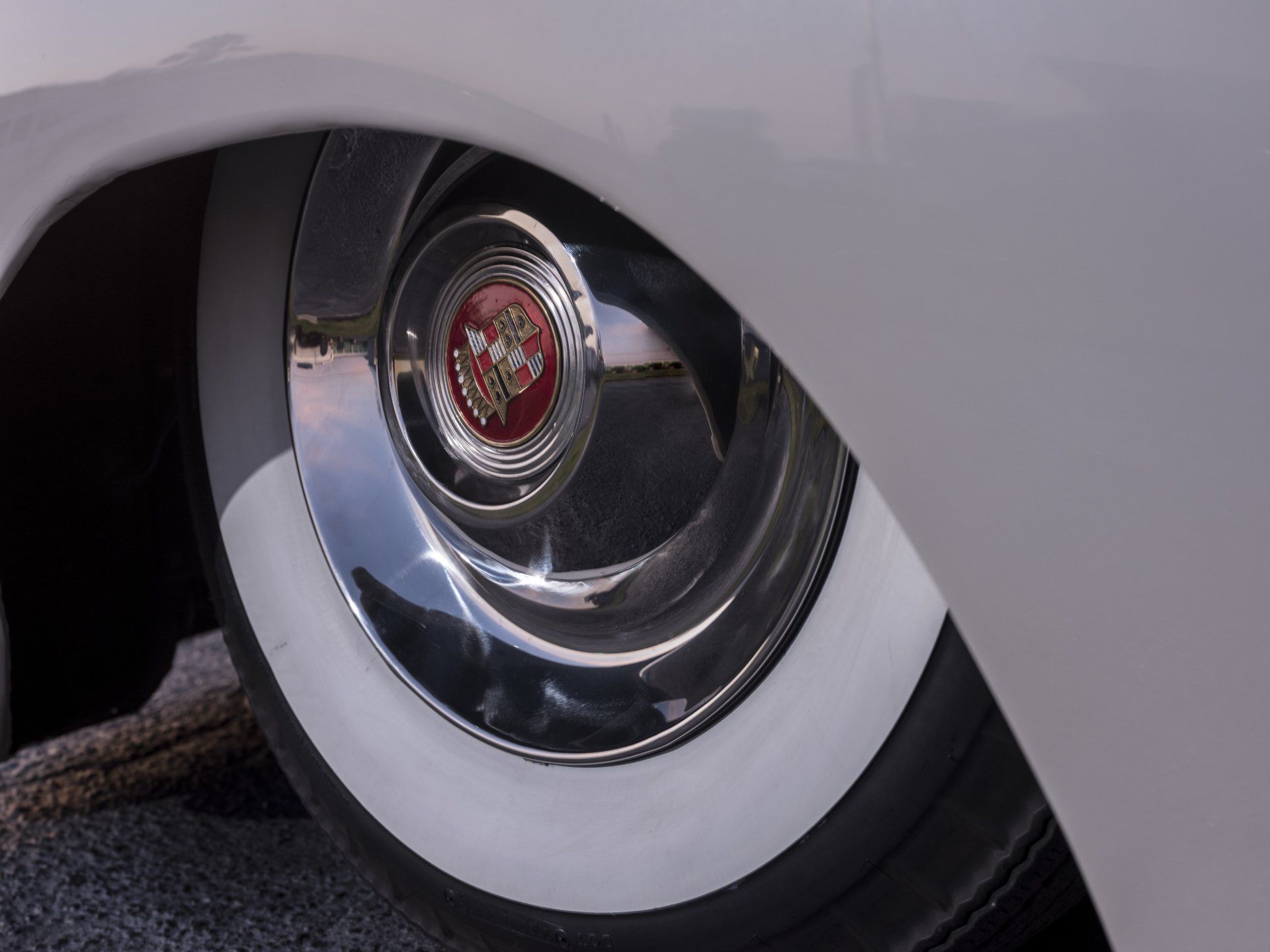 Close-up of a classic car wheel with a whitewall tire and chrome hubcap