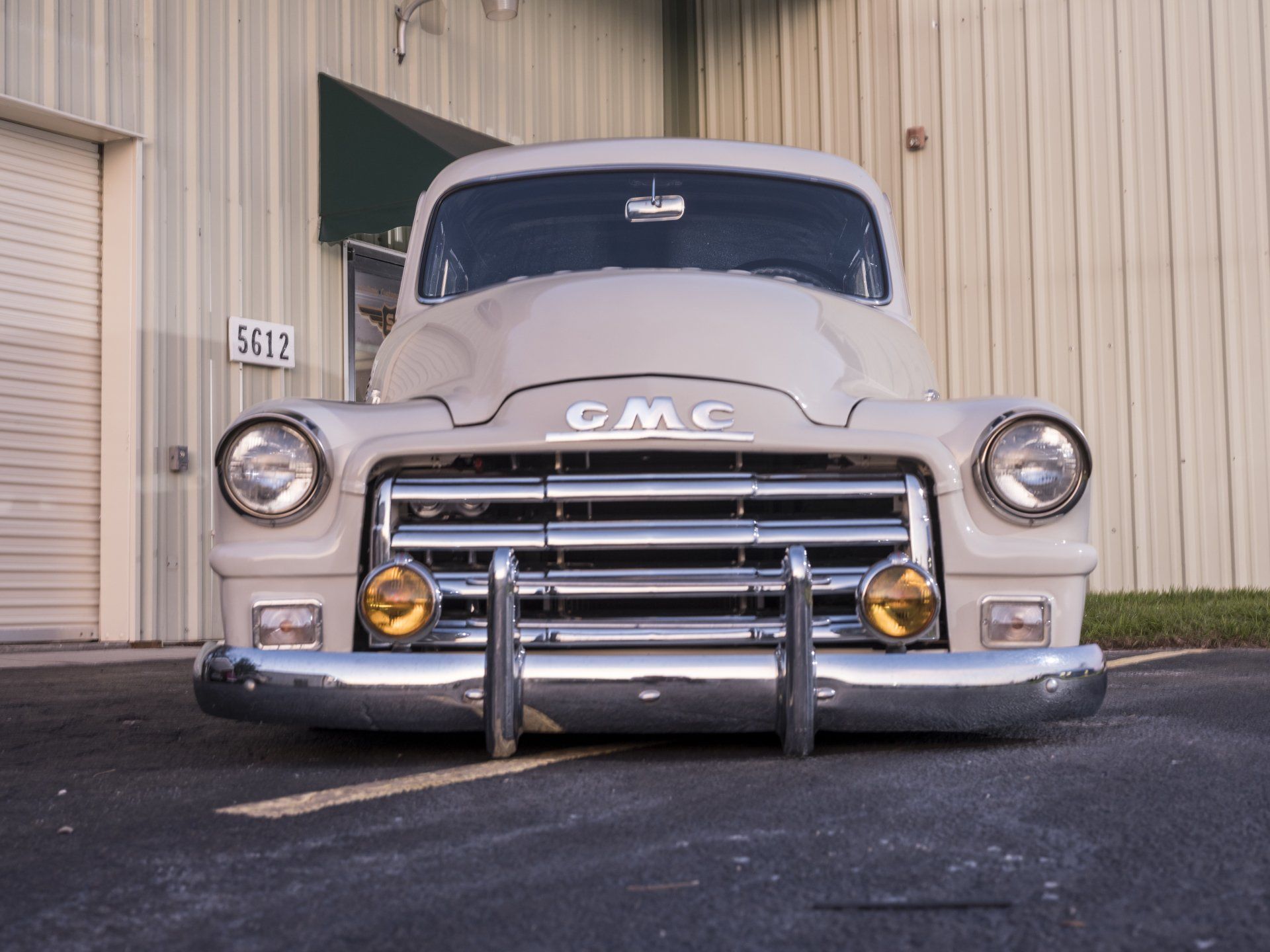 Front view of a beige GMC pickup truck parked outside a metal building