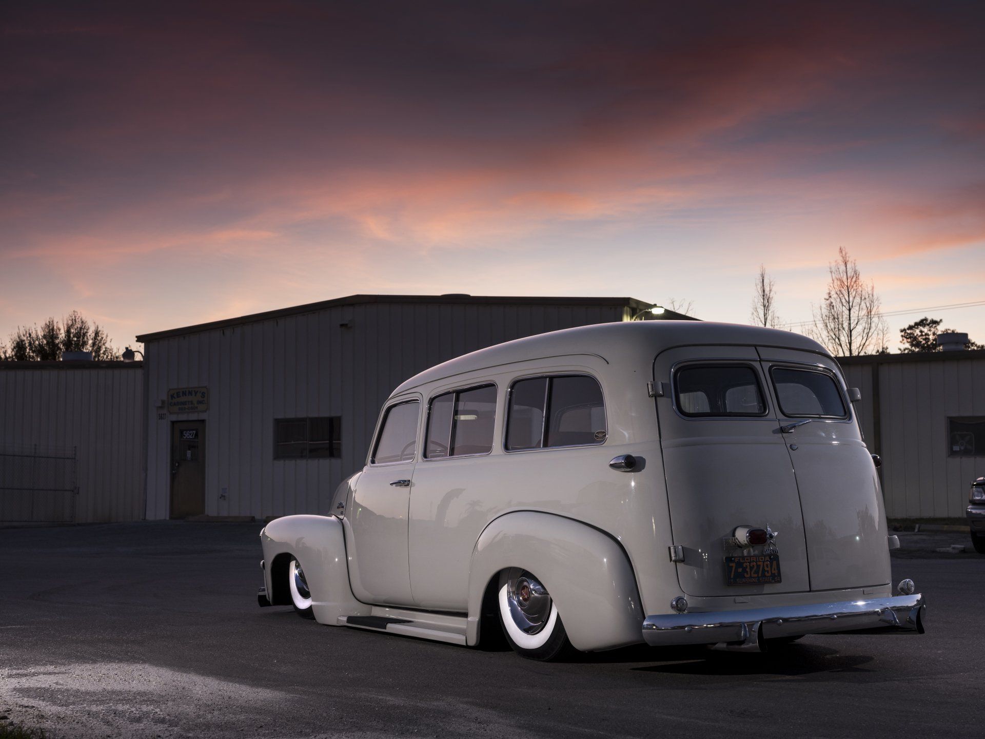 Vintage white sedan parked outside a building at dusk under a pink-purple sky