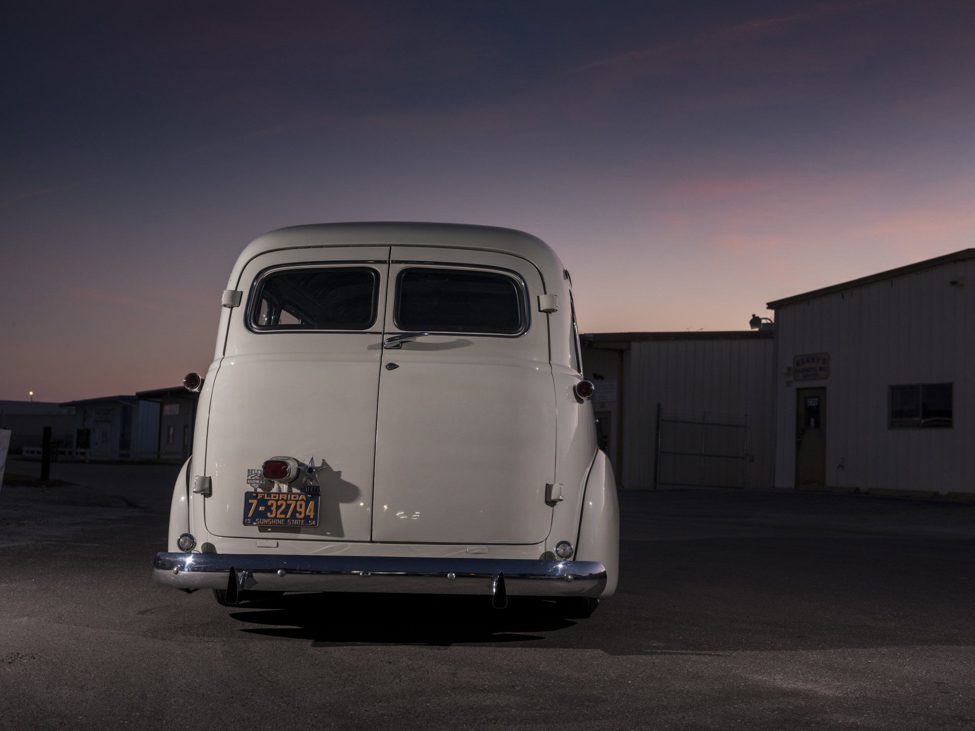 Rear view of a white vintage car parked on a lot at dusk