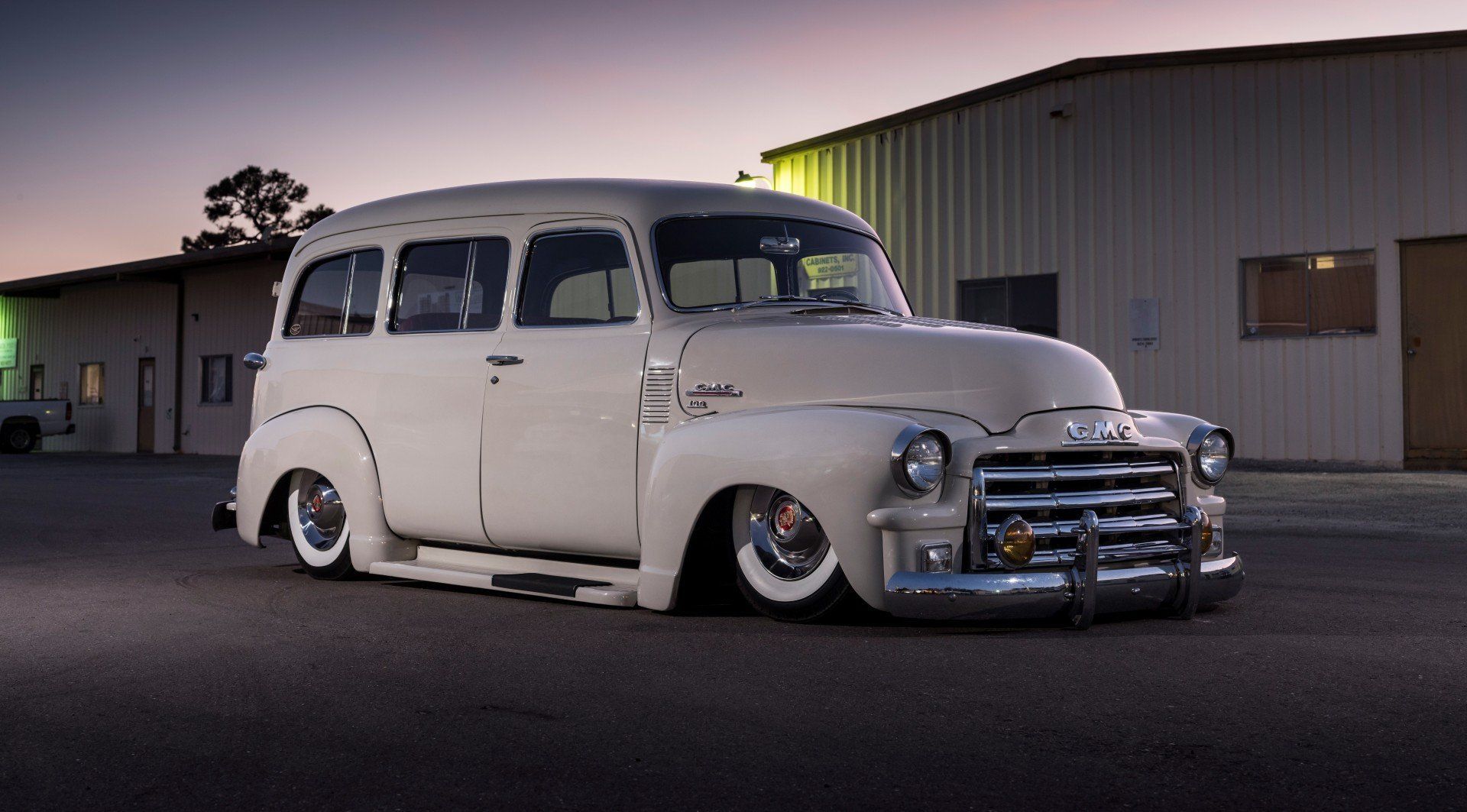 Classic white vintage station wagon with chrome grille parked outdoors at dusk near an industrial building