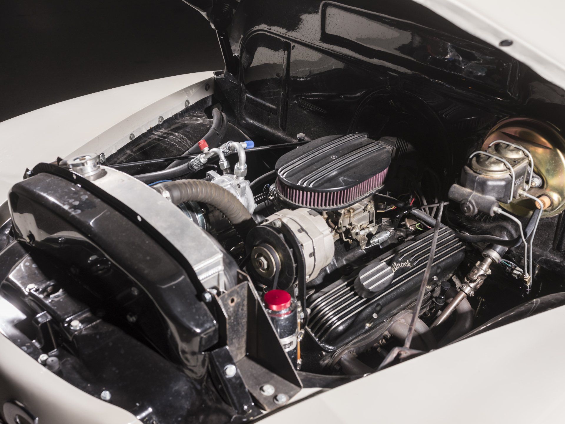 Classic car engine bay with chrome parts, black valve covers, and a polished air intake under an open hood