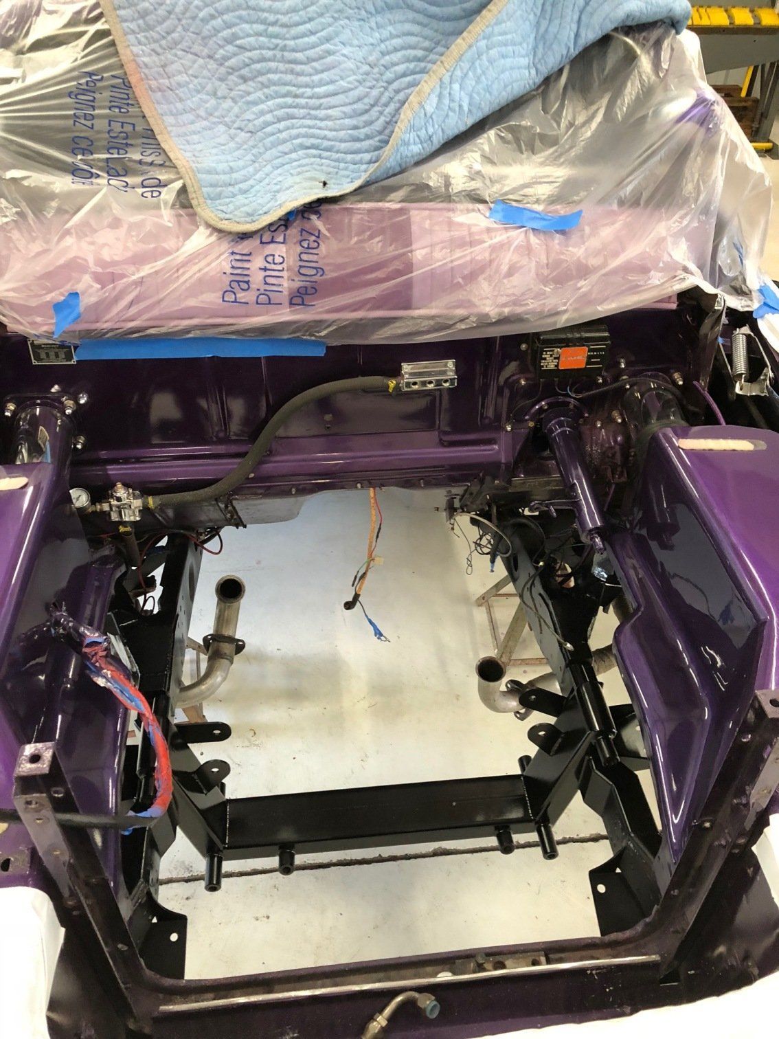 Purple car chassis interior with exposed frame, wiring, and a covered seat area under repair