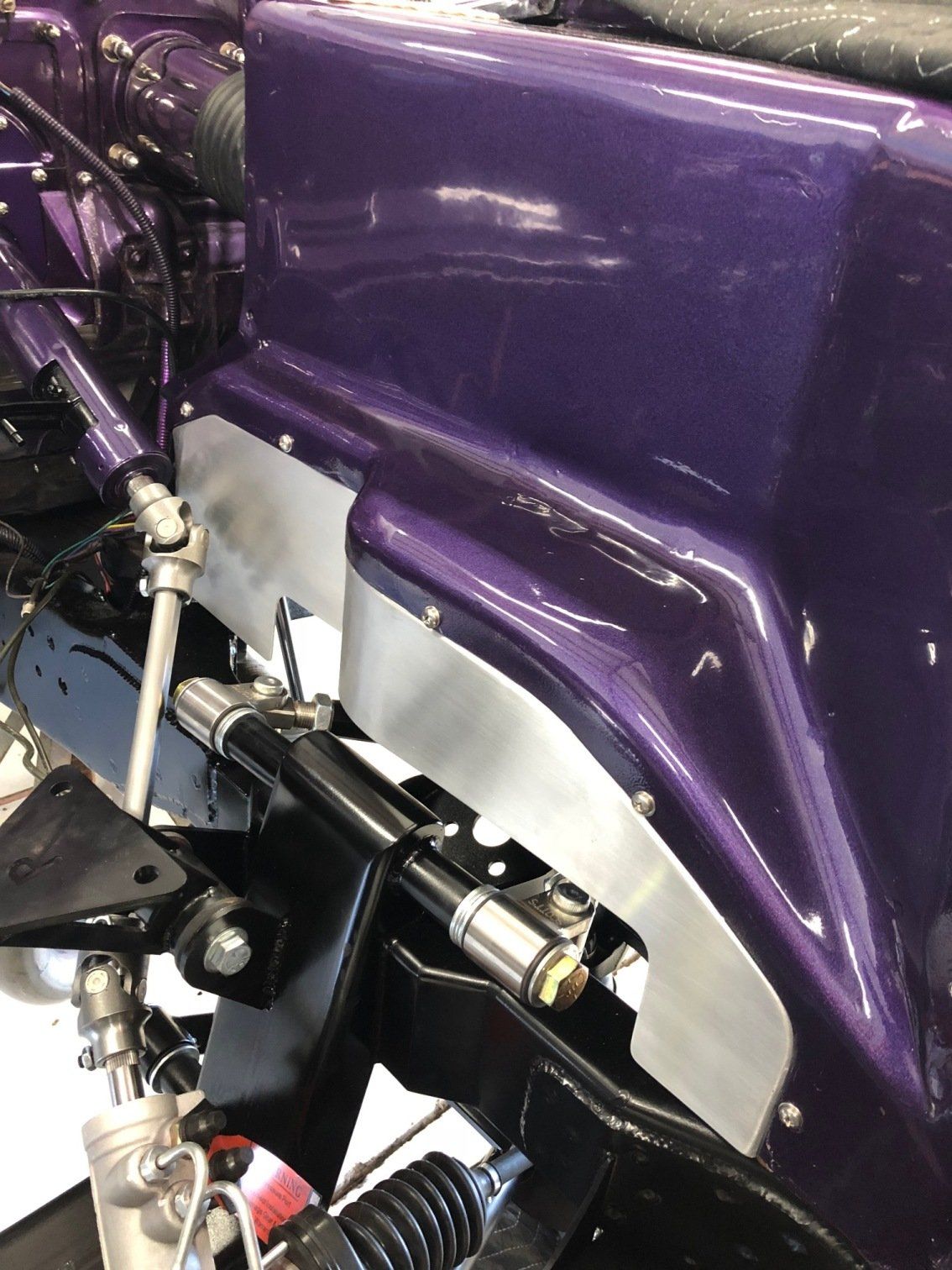 Close-up of a purple car body panel and mechanical components in an automotive workshop