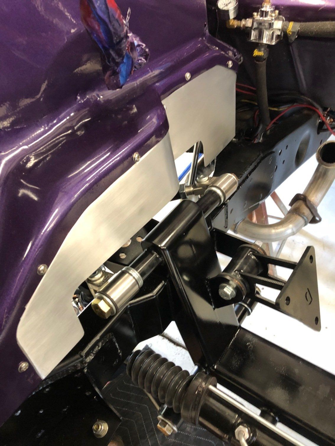 Close-up of a car chassis with purple body panels, metal brackets, wiring, and suspension components