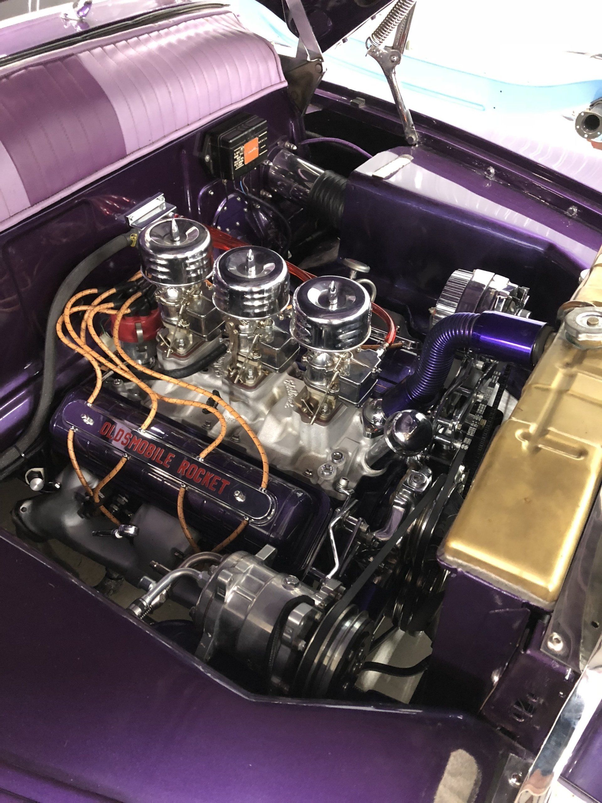 Purple car engine bay with polished triple carburetors and chrome parts, viewed from above