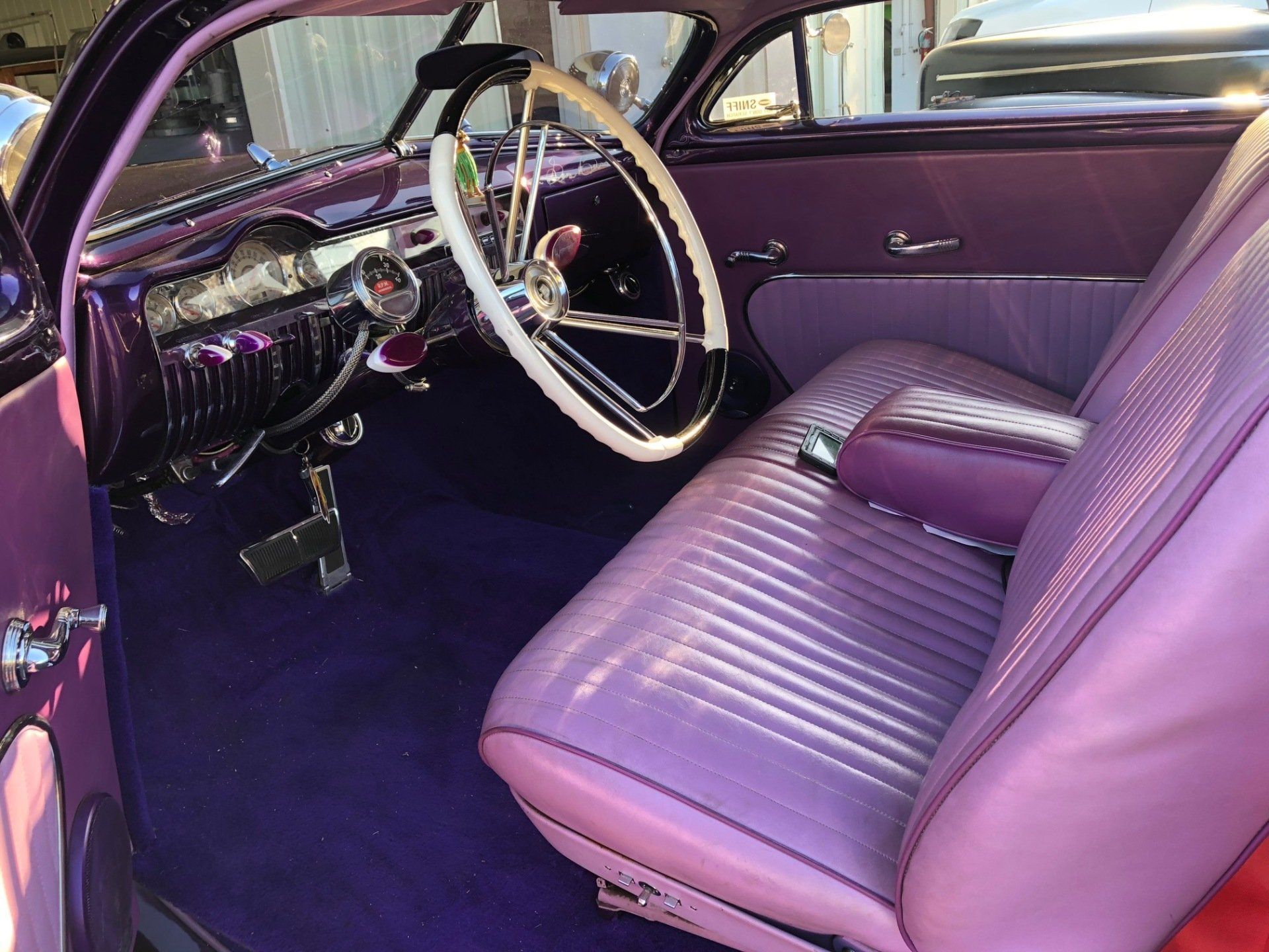 Classic car interior with purple upholstery, white steering wheel, and dashboard on display