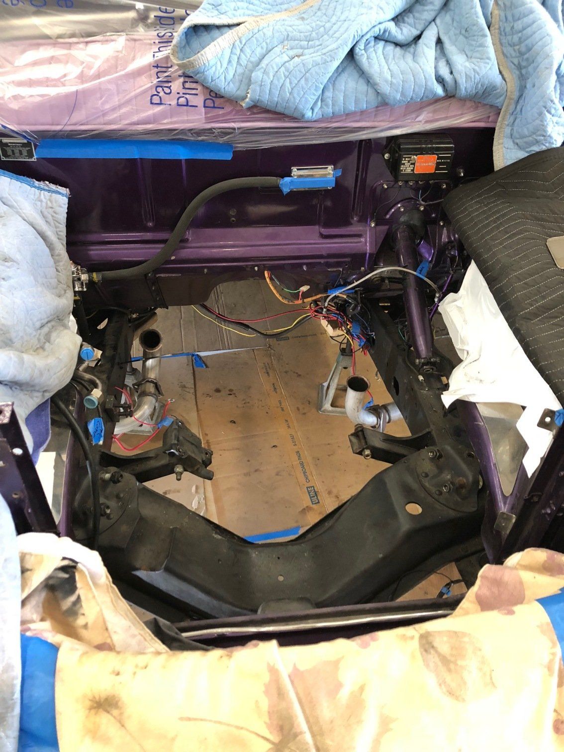 Car interior stripped to bare metal with exposed wiring and removed seats, showing repair or restoration work