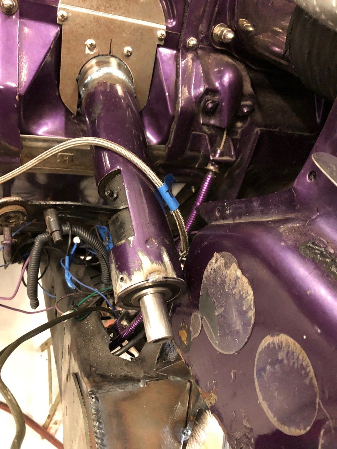 Close-up of purple car engine bay with chrome pipework, hoses, and worn paint panels.