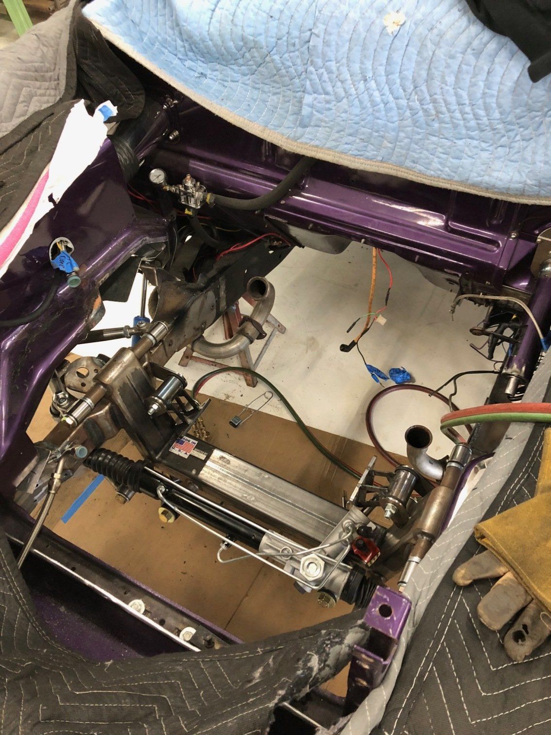 Interior of a purple-framed vehicle, showing exposed wiring, mechanical parts, and white floor panels under repair.