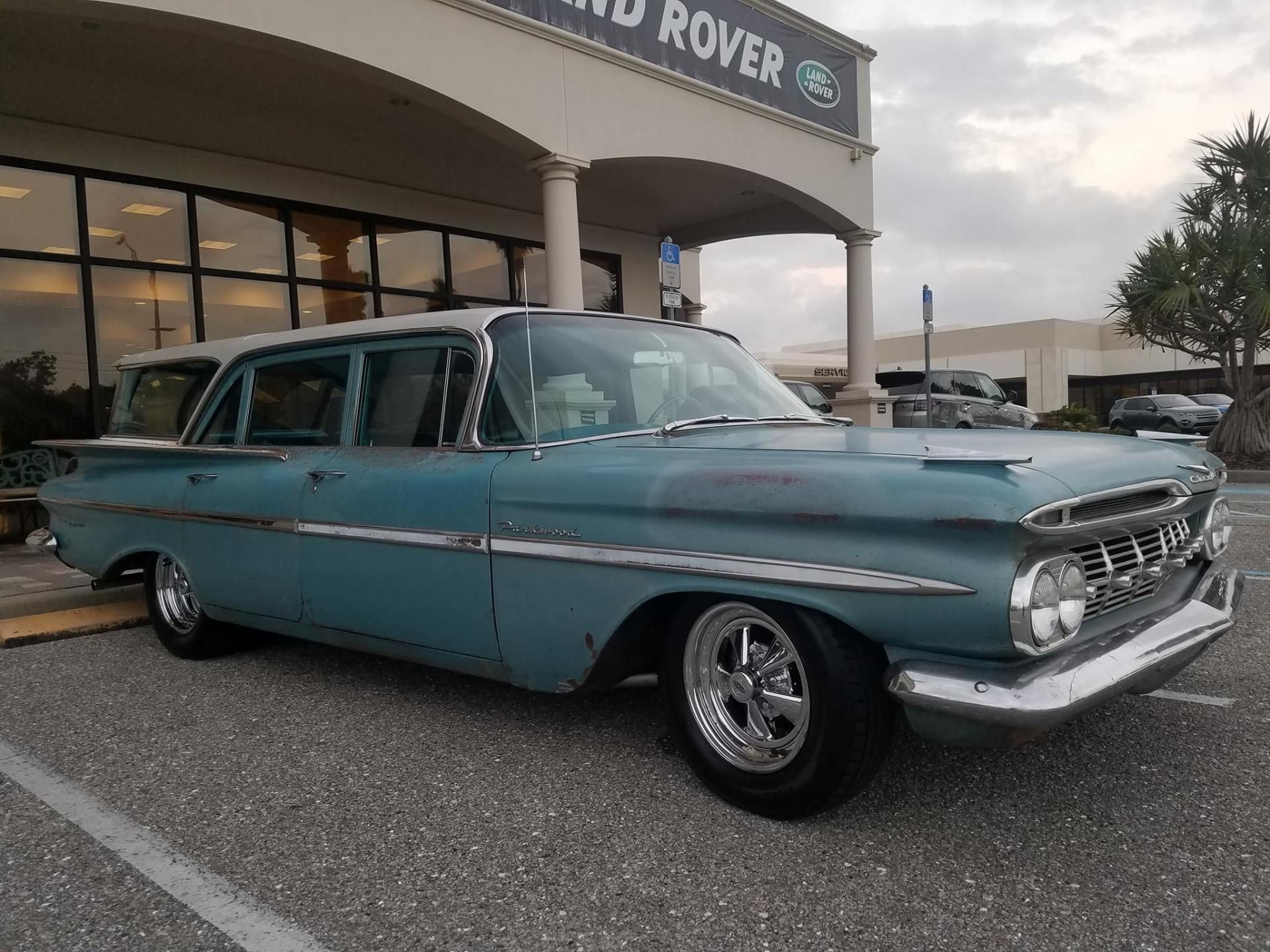 Vintage turquoise station wagon parked at a dealership under an awning