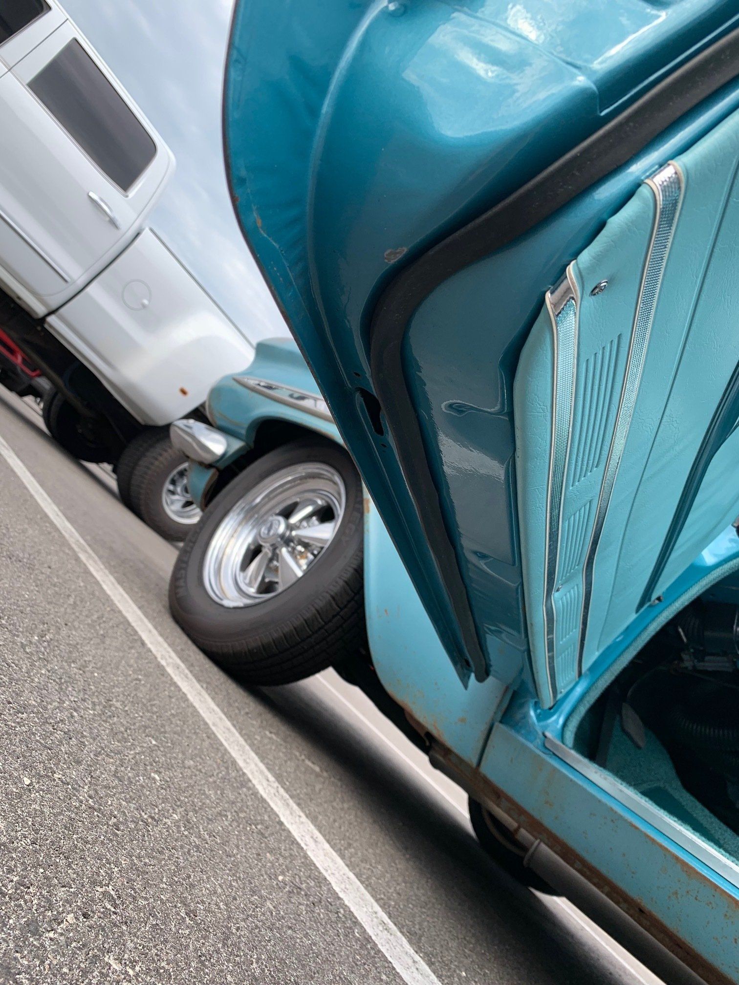 Vintage teal car parked close to a white truck along a street curb