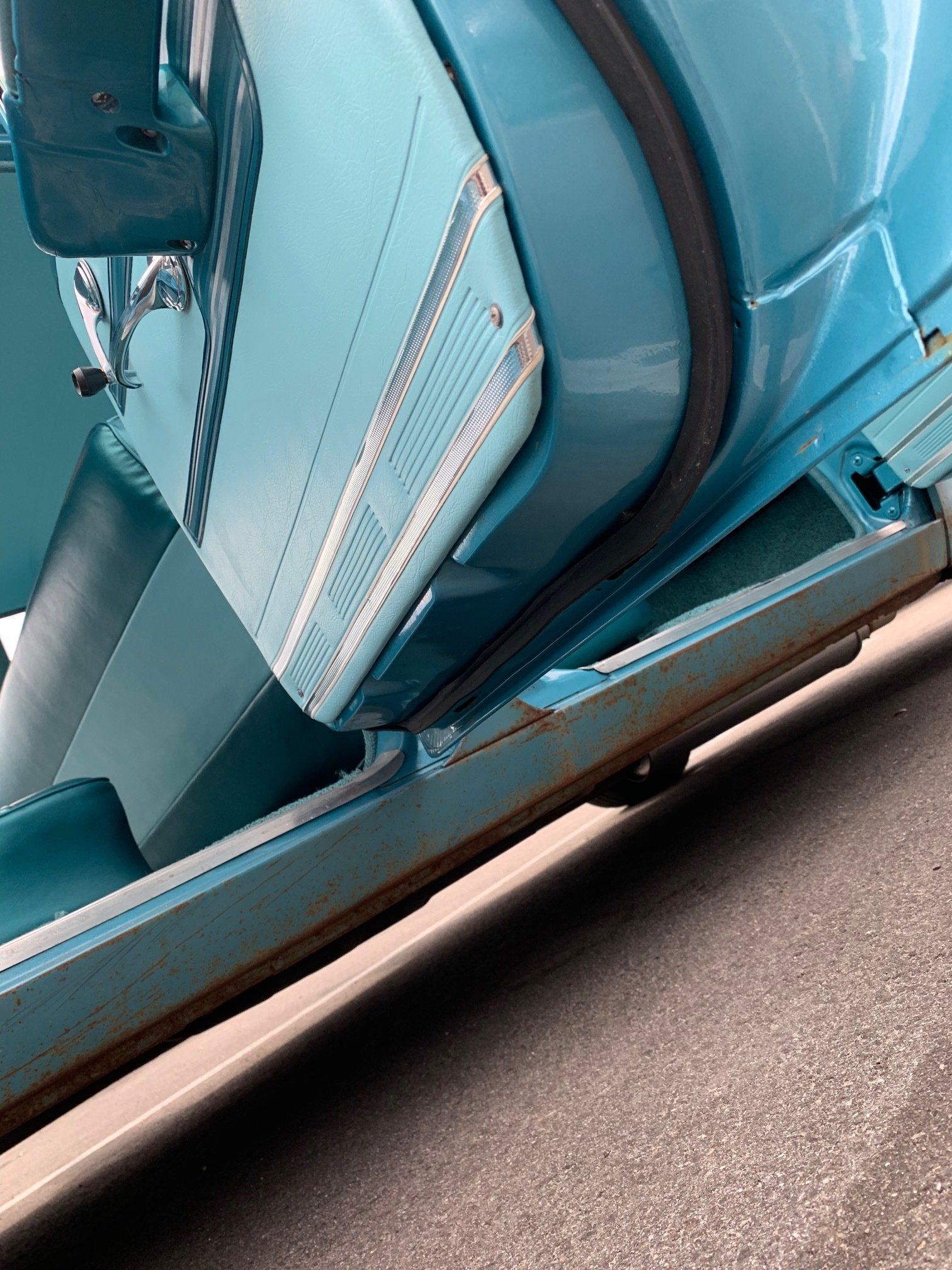 Close-up of a turquoise vintage car door and side panel on pavement