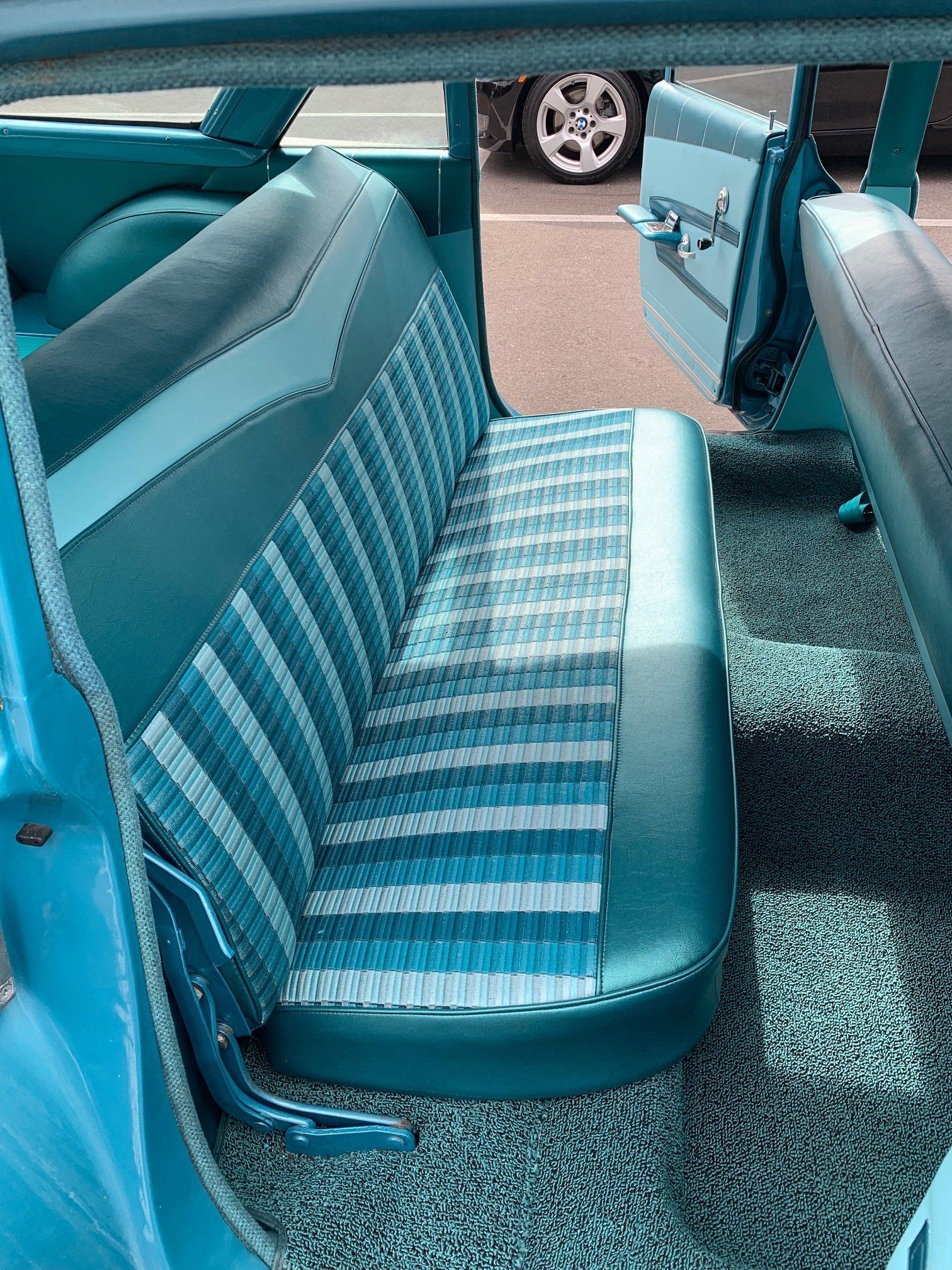 Turquoise car interior with striped bench seat and open rear door, showing pavement outside