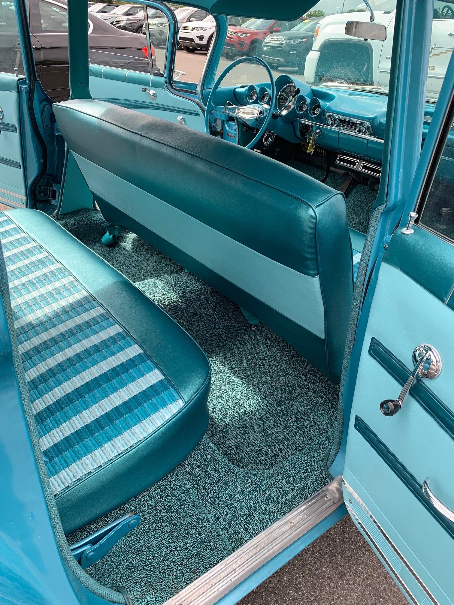 Teal vintage car interior with bench seats and patterned floor mat, viewed from the back seat