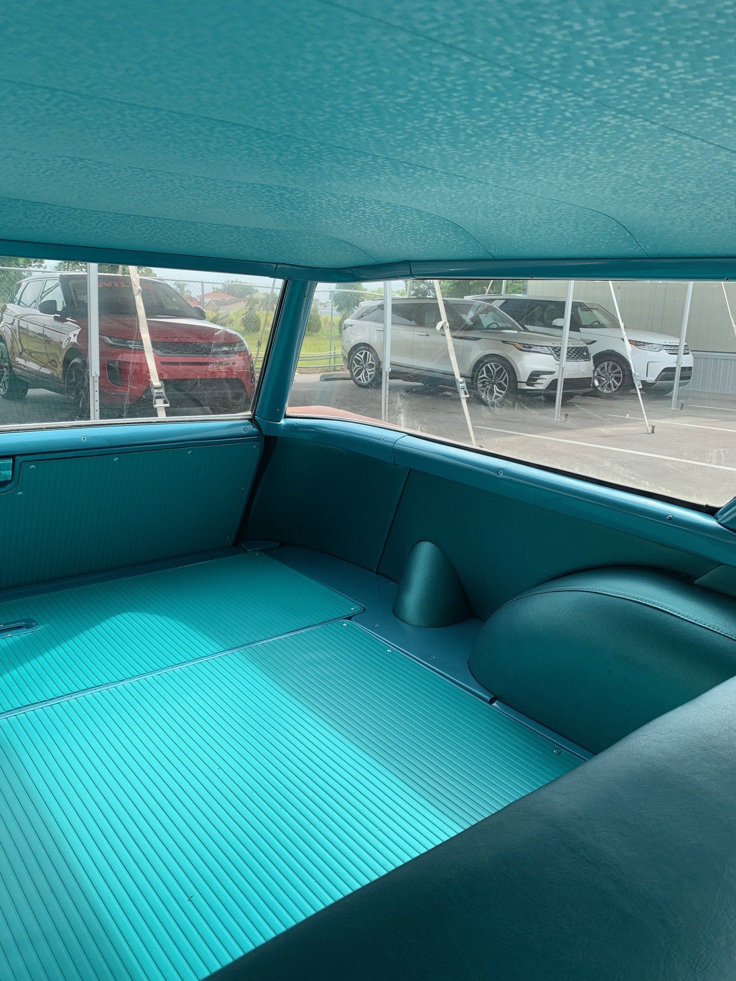 Turquoise car interior with a rear bench seat and rear window view of parked vehicles